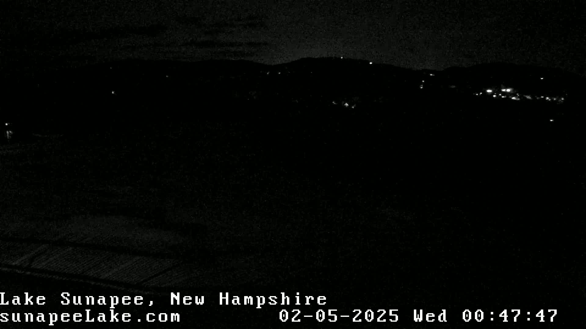 A nighttime, dark view of a hilly landscape with a few distant lights.