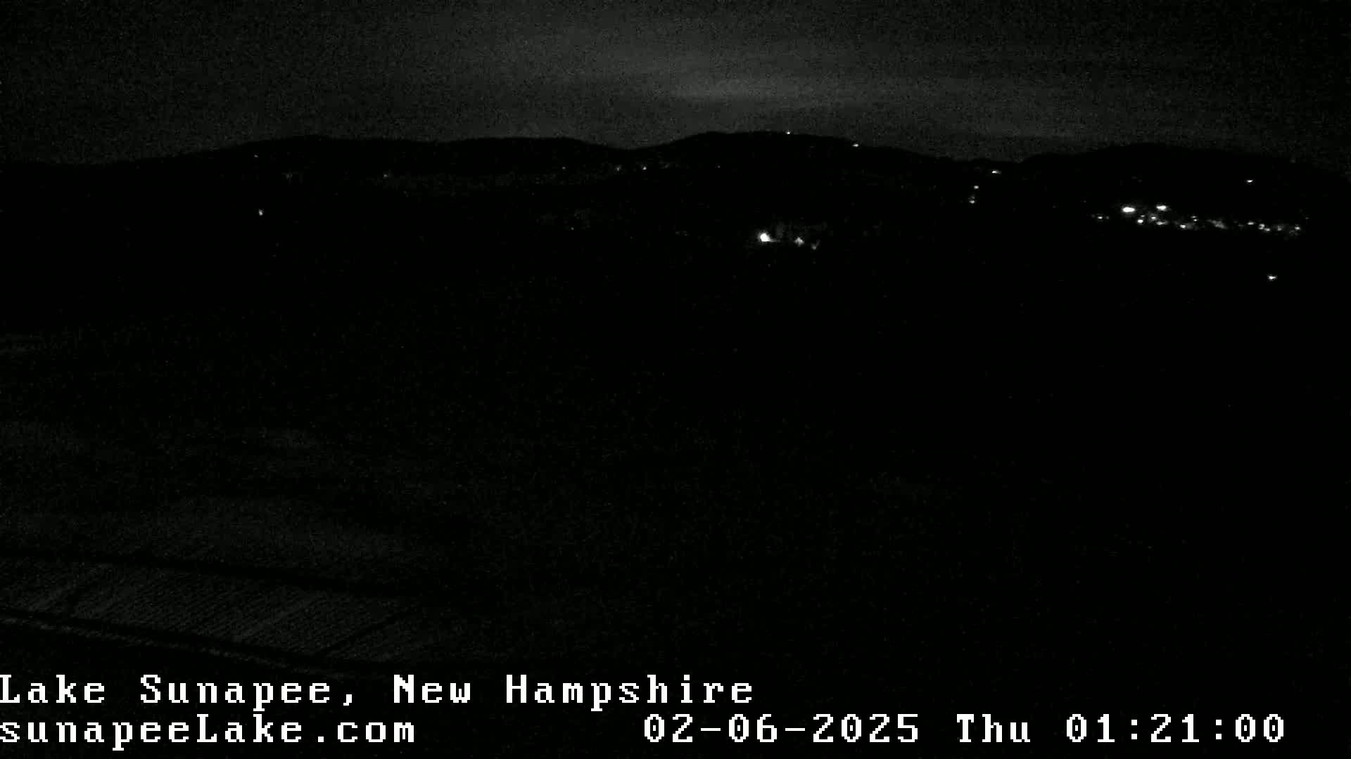 A nighttime, dark view of dimly lit hills and a few scattered lights.