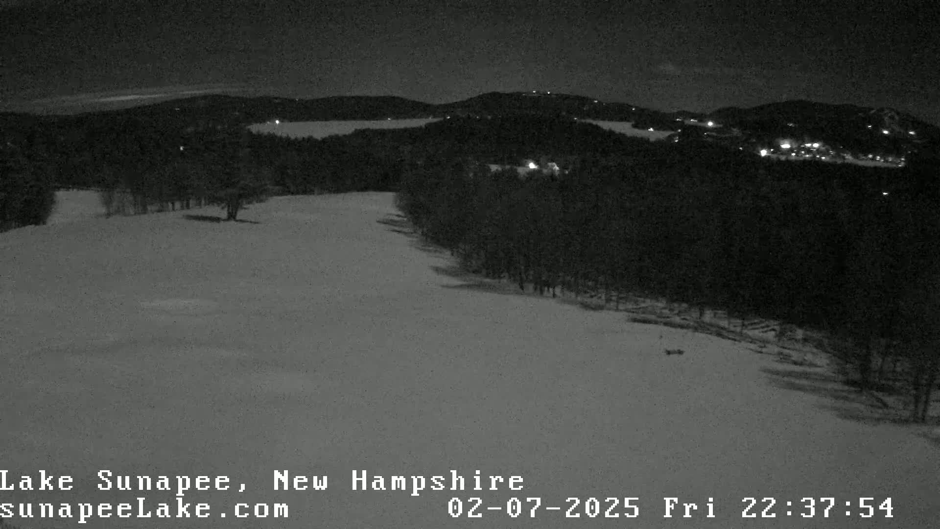 A snow-covered landscape at night, with a few distant lights visible in the background.