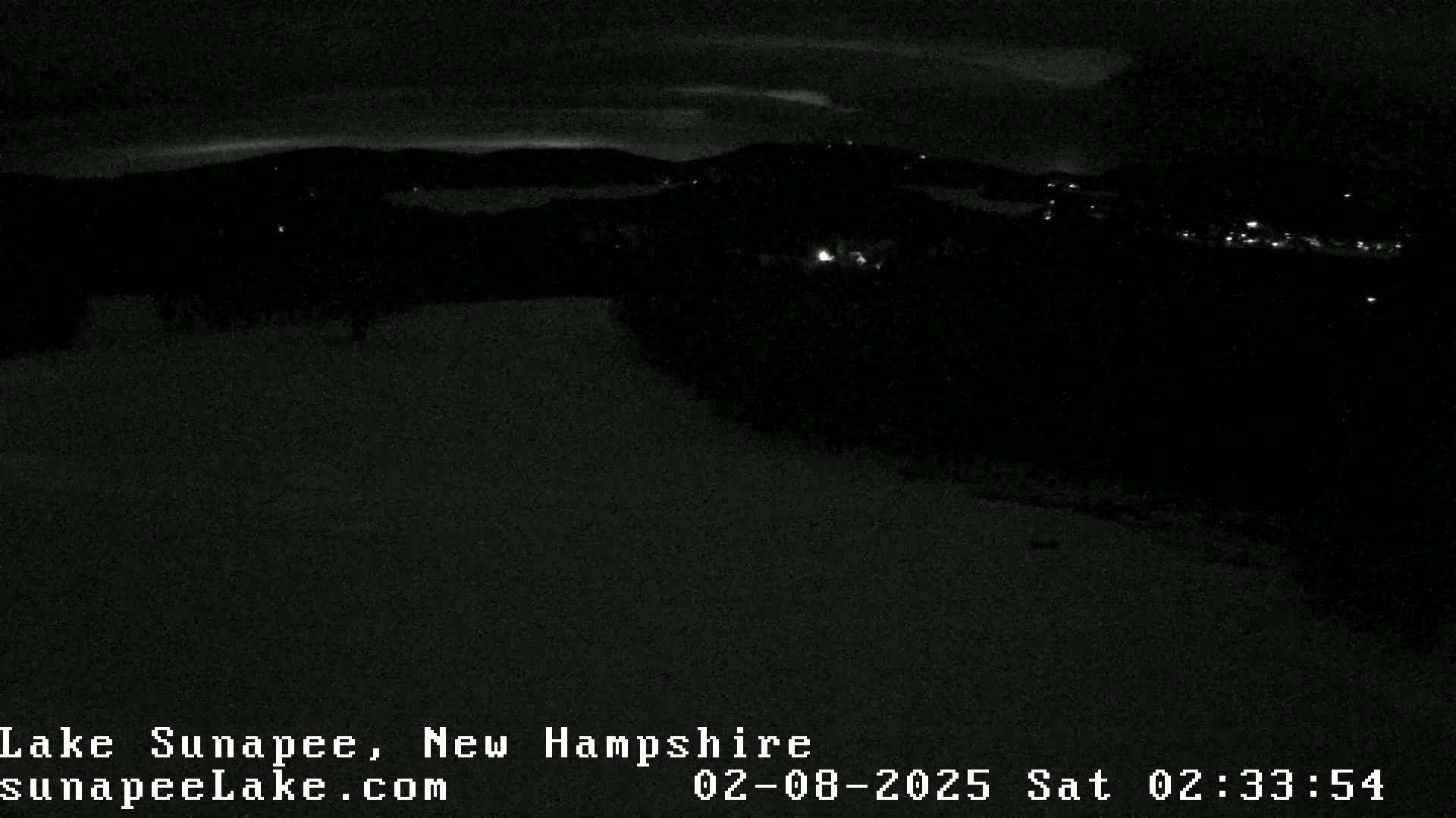 A nighttime, low-light view of a snow-covered landscape with distant lights from a town or village.