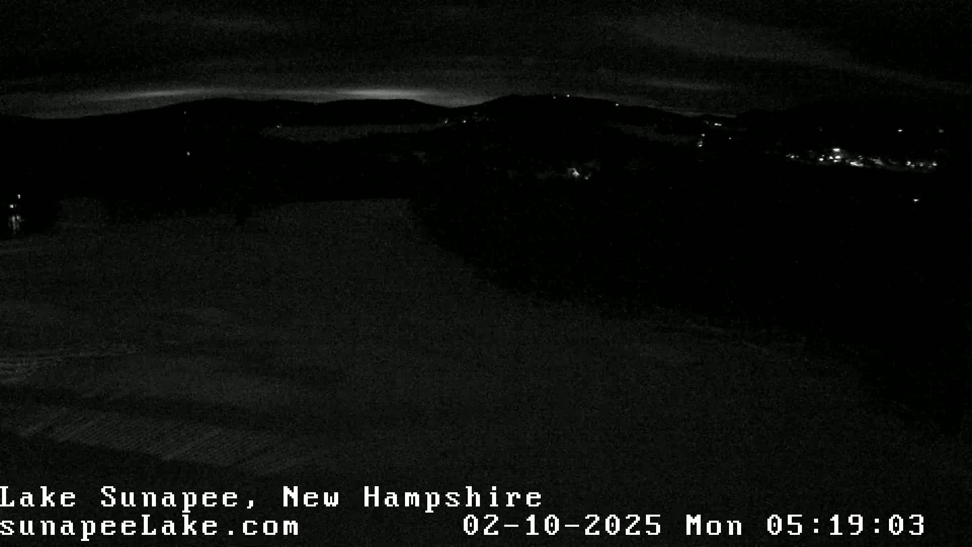 A nighttime view of a snow-covered landscape with a few distant lights visible under a dark sky.