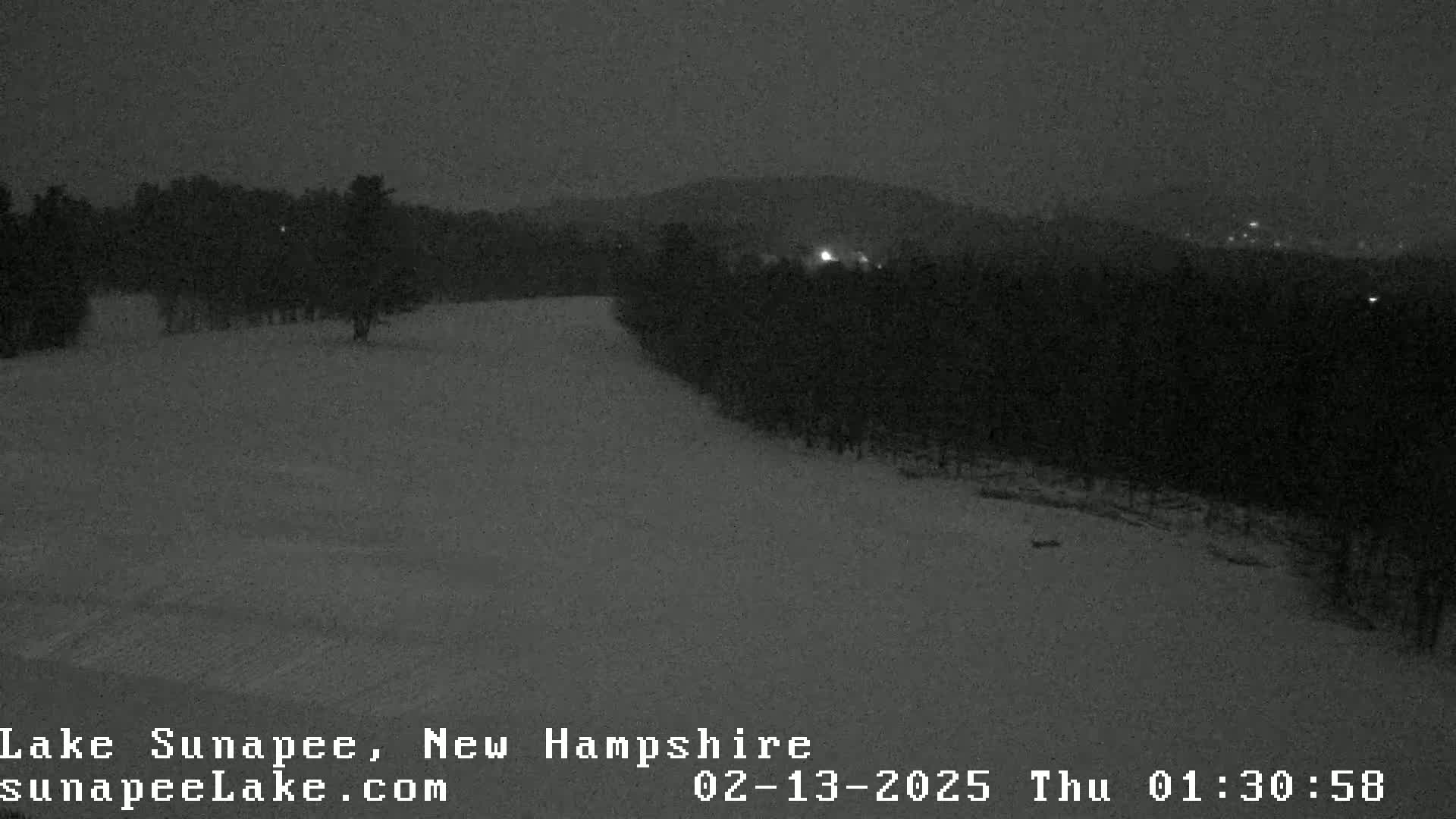 A snow-covered landscape at night, with a dark forest in the background under a dark sky.