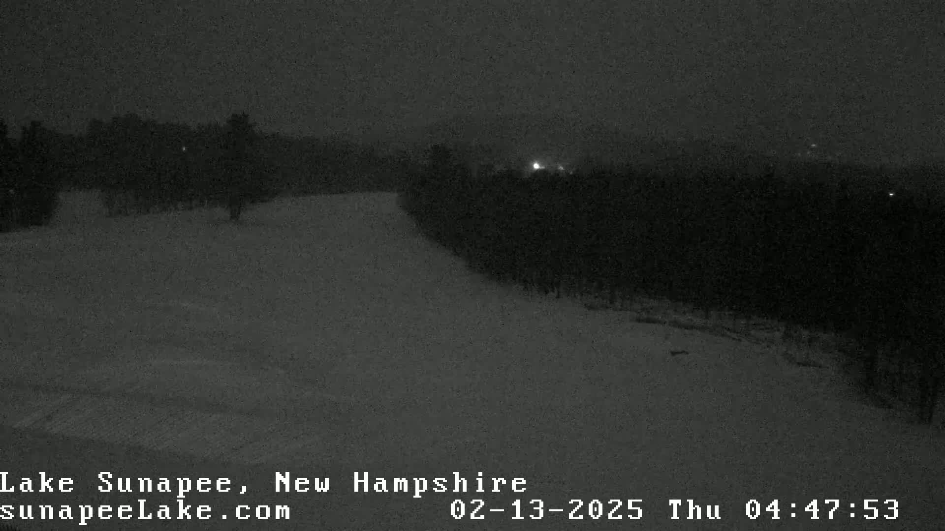 A snow-covered landscape at night, with a dark forest in the background under a dark sky.