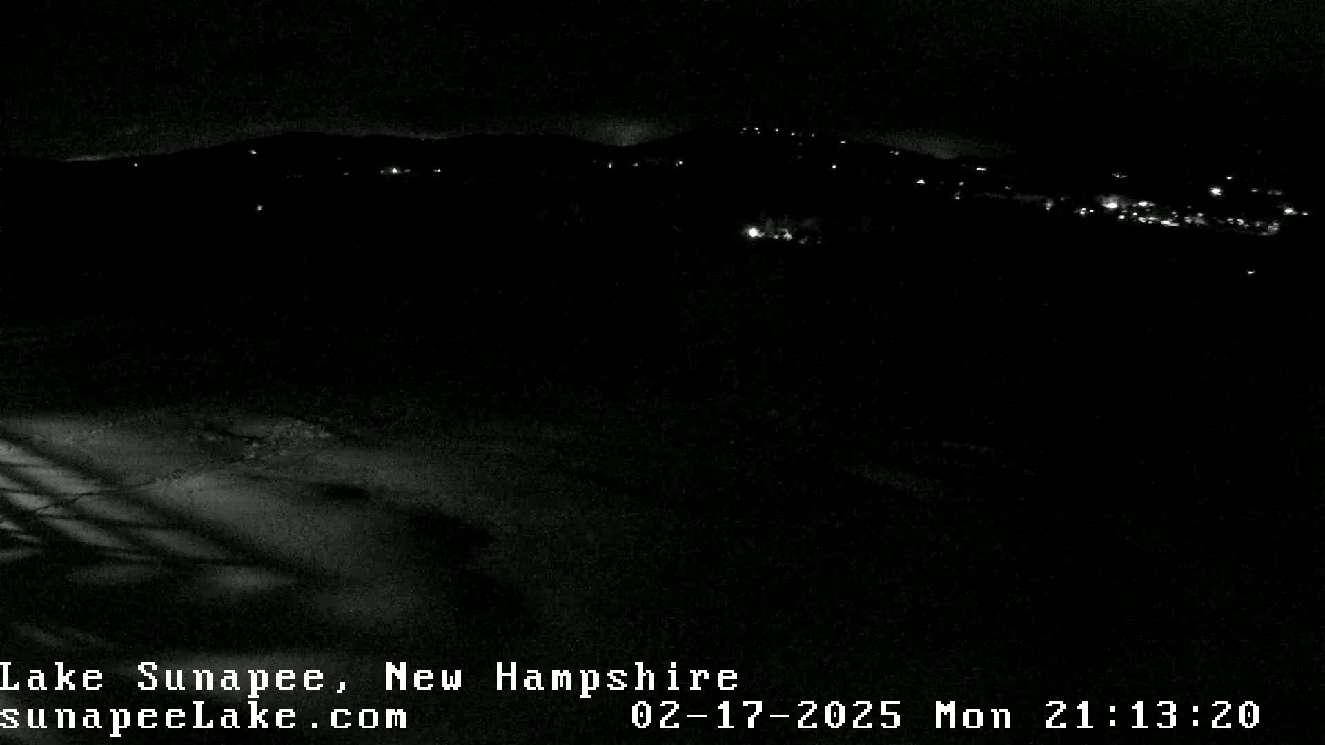 A nighttime, snow-covered landscape shows a distant hillside with scattered lights.