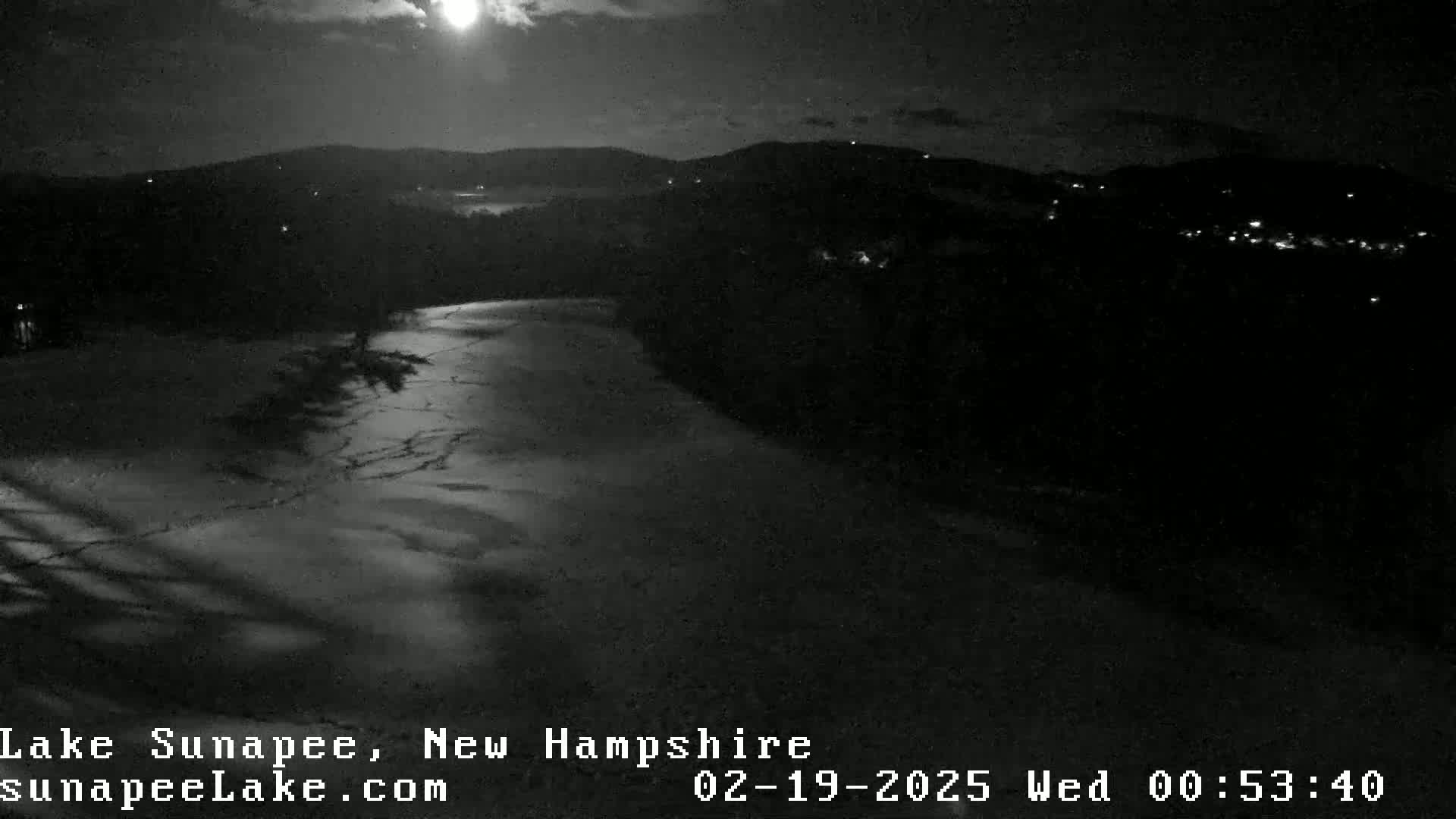 A nighttime, moonlit view of a partially frozen lake and dark, hilly landscape.
