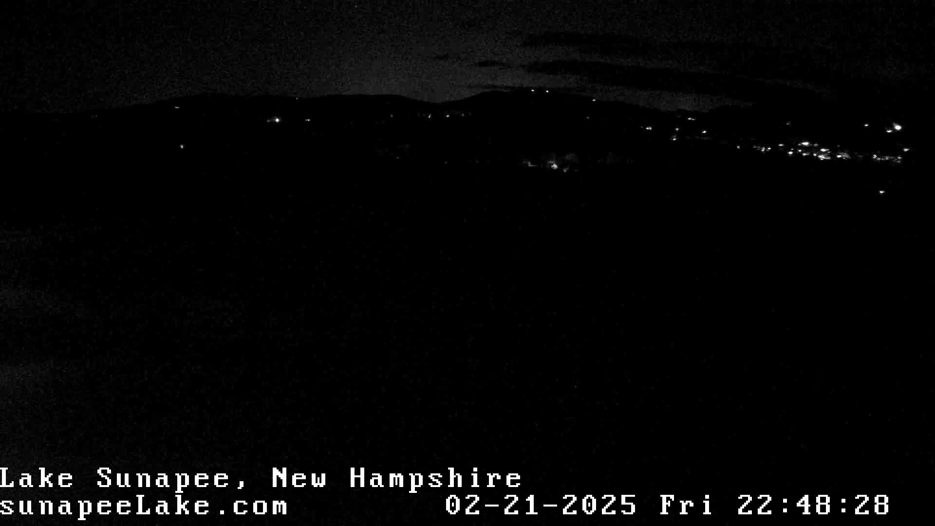 A nighttime, long-range view of a distant town or village with scattered lights illuminated against a dark, mostly clear sky.