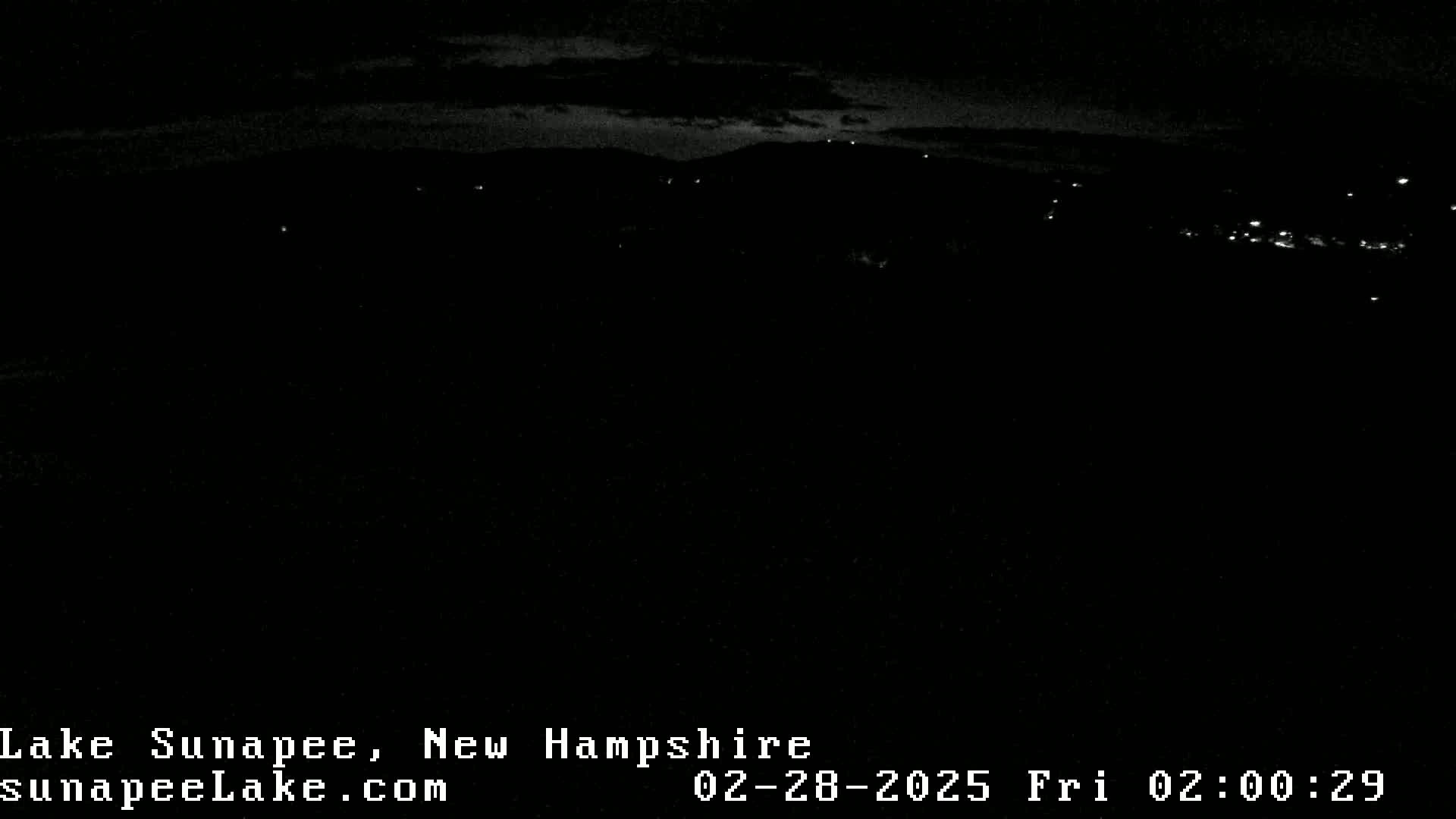 A nighttime long shot shows a dark landscape with a few faint lights in the distance under a mostly clear, dark sky.