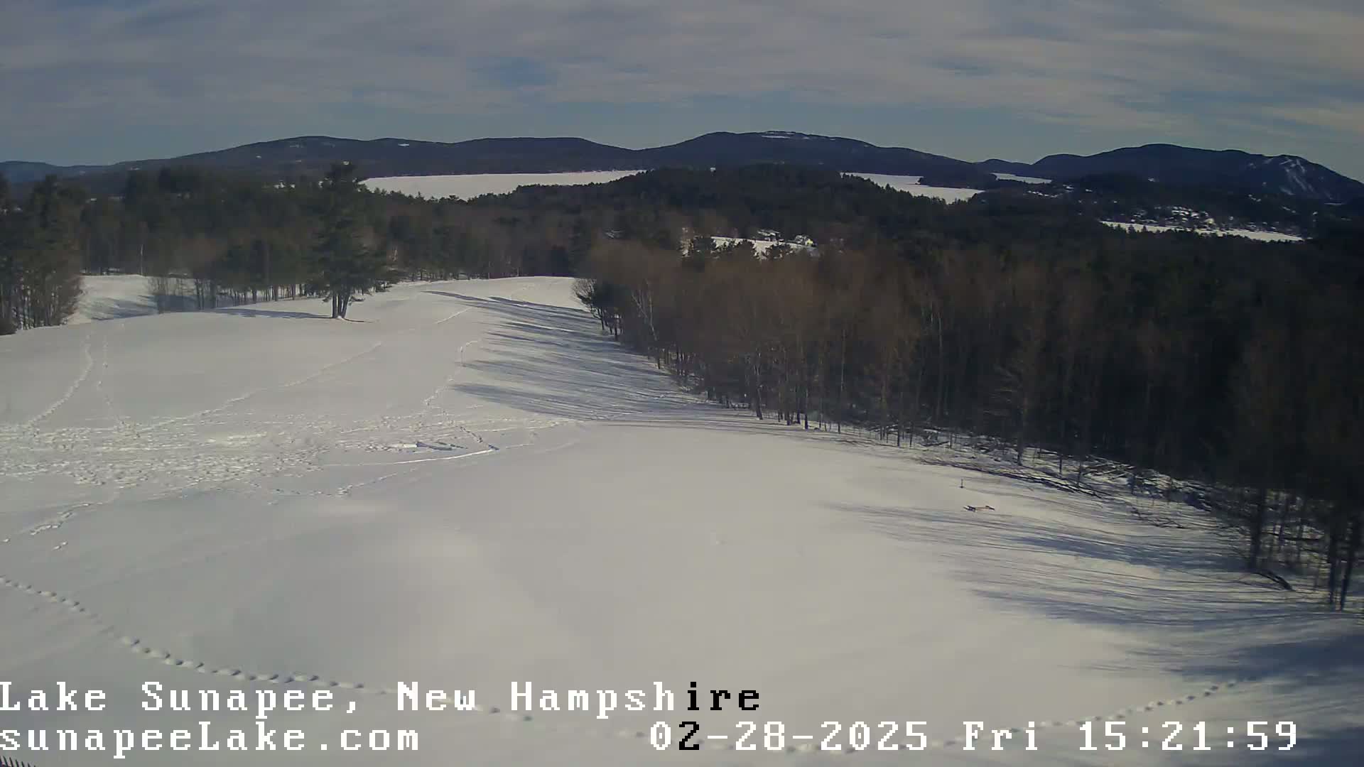 A snow-covered landscape with a forest and distant mountains under a mostly clear sky.