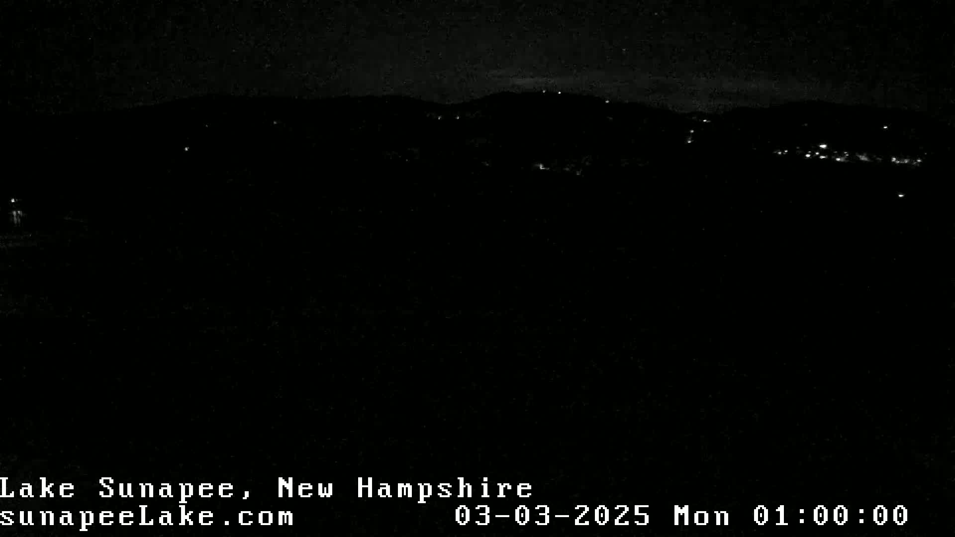 A nighttime view of a dark landscape with scattered lights in the distance under a clear sky.