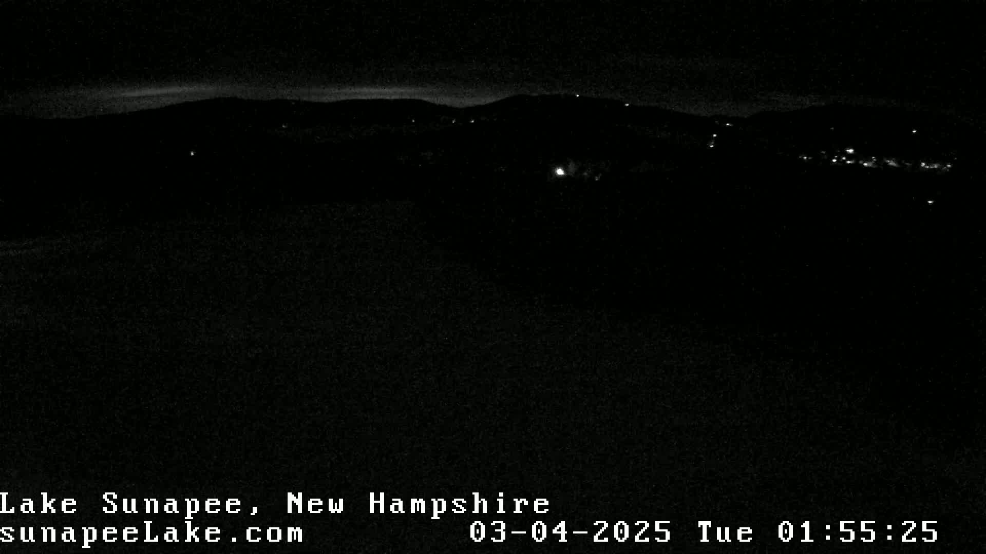 A nighttime, dark view of a distant town nestled in hills under a clear sky.