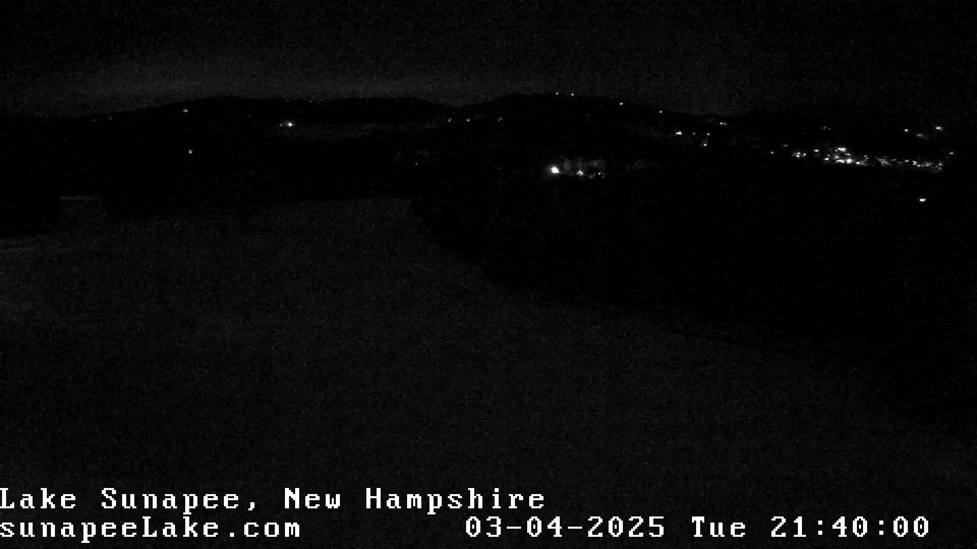 A nighttime, low-light view of a distant town or village, illuminated by scattered lights, against a dark sky.