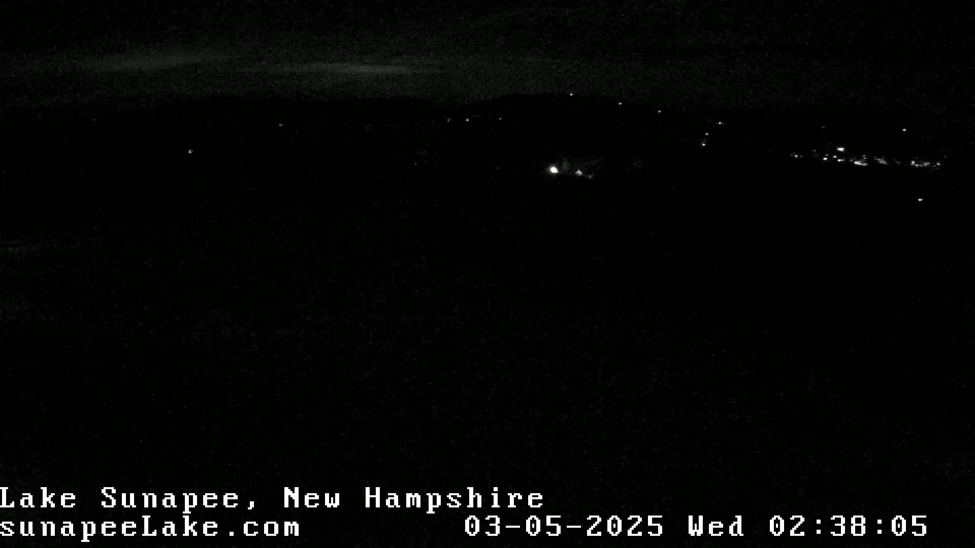 A nighttime long shot of a dark landscape with a few distant lights.