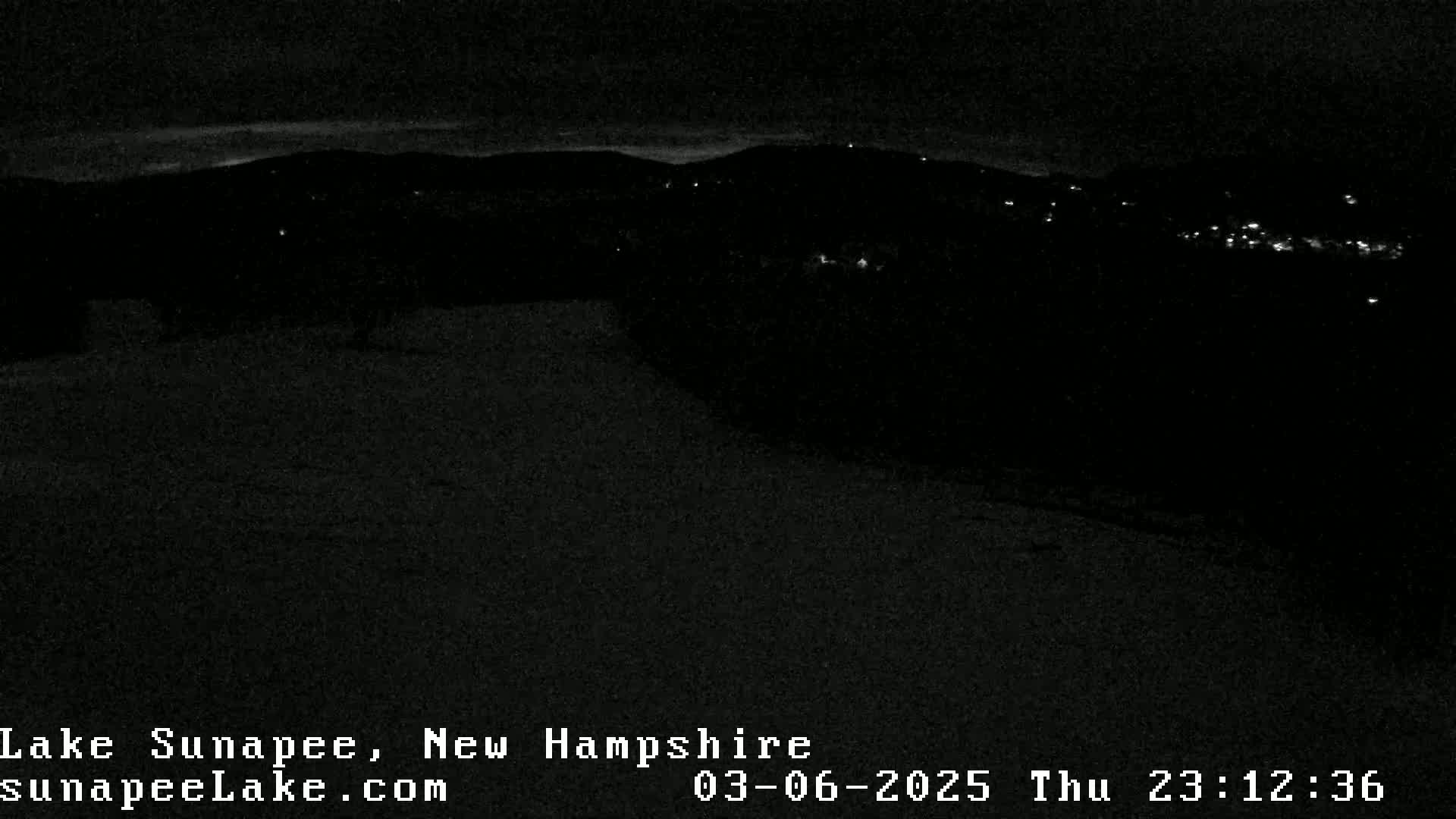 A nighttime, low-light view of a dark landscape with distant lights and a hint of a snowy or icy foreground.