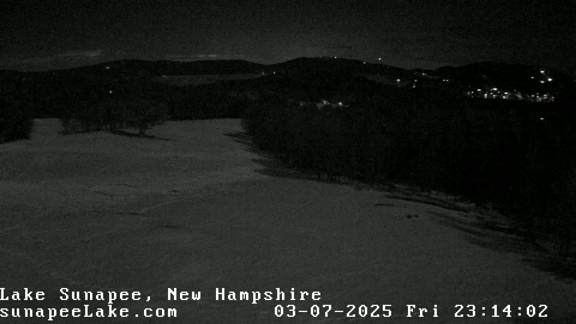 A nighttime, snow-covered landscape with a few distant lights visible in the hills.