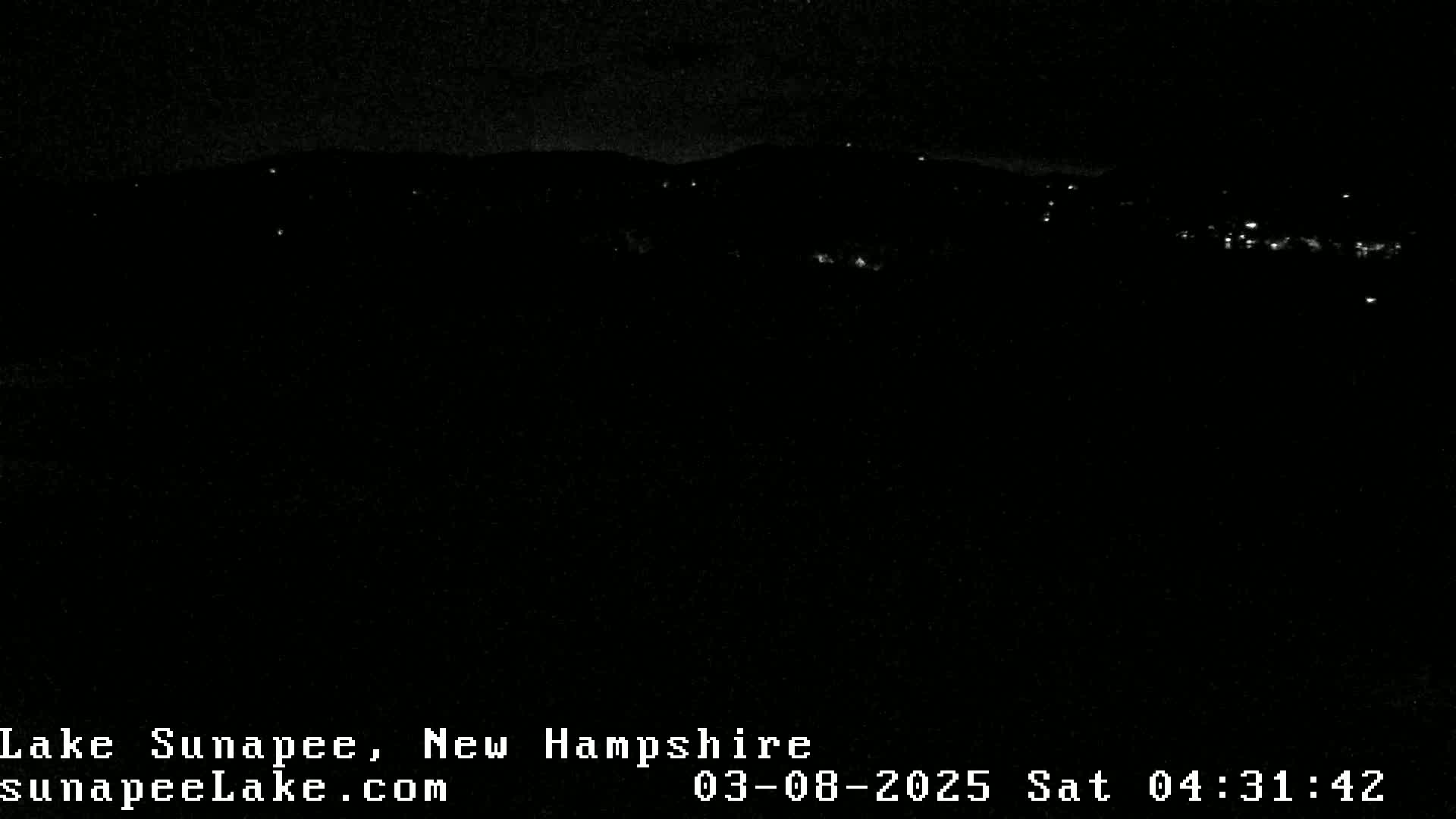 A nighttime view of a dark landscape with sparsely scattered lights in the distance under a clear, dark sky.