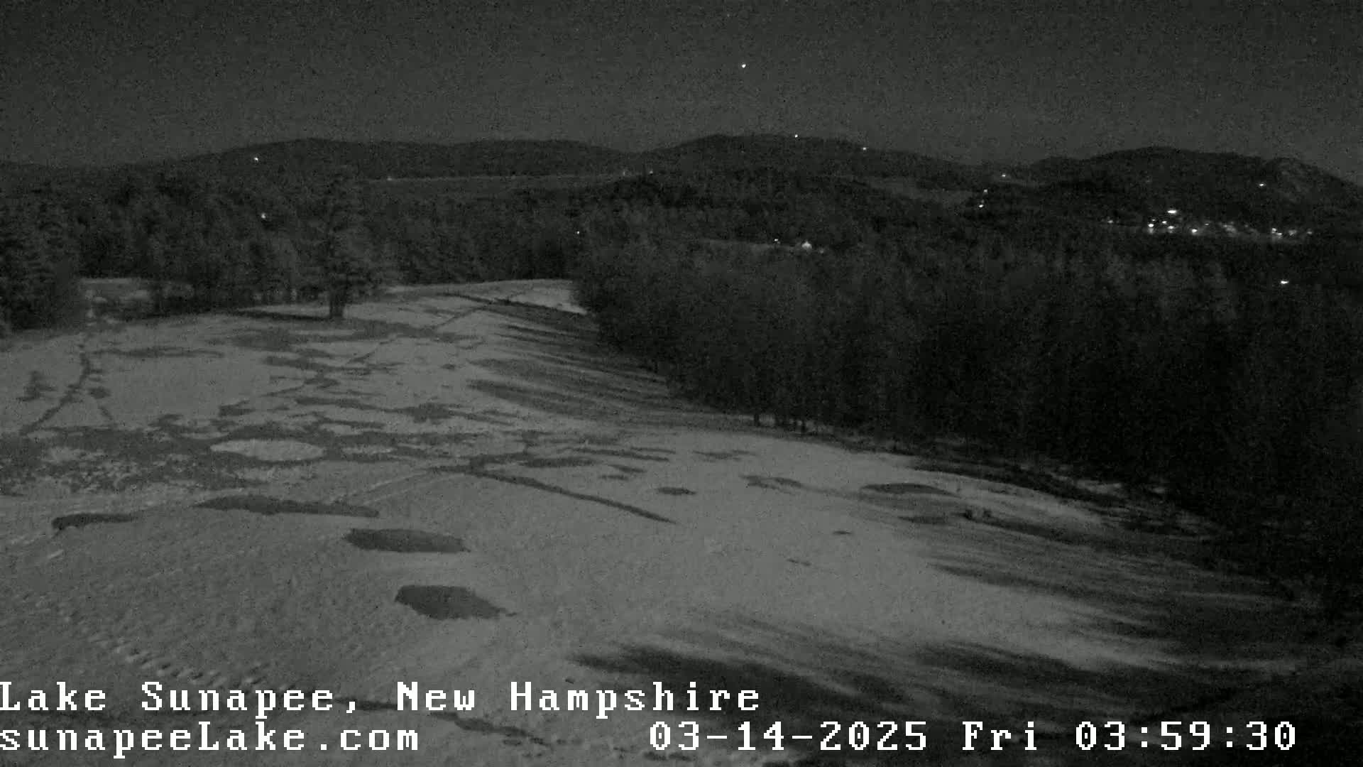 A snow-covered landscape at night, with a dark forest in the background under a clear sky.