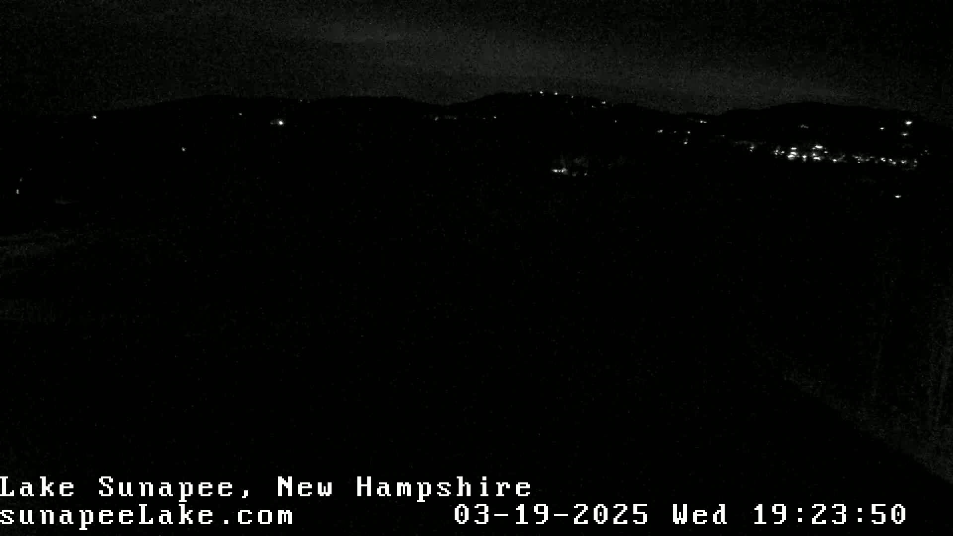 A nighttime, dark view of a distant hillside with sparsely scattered lights.