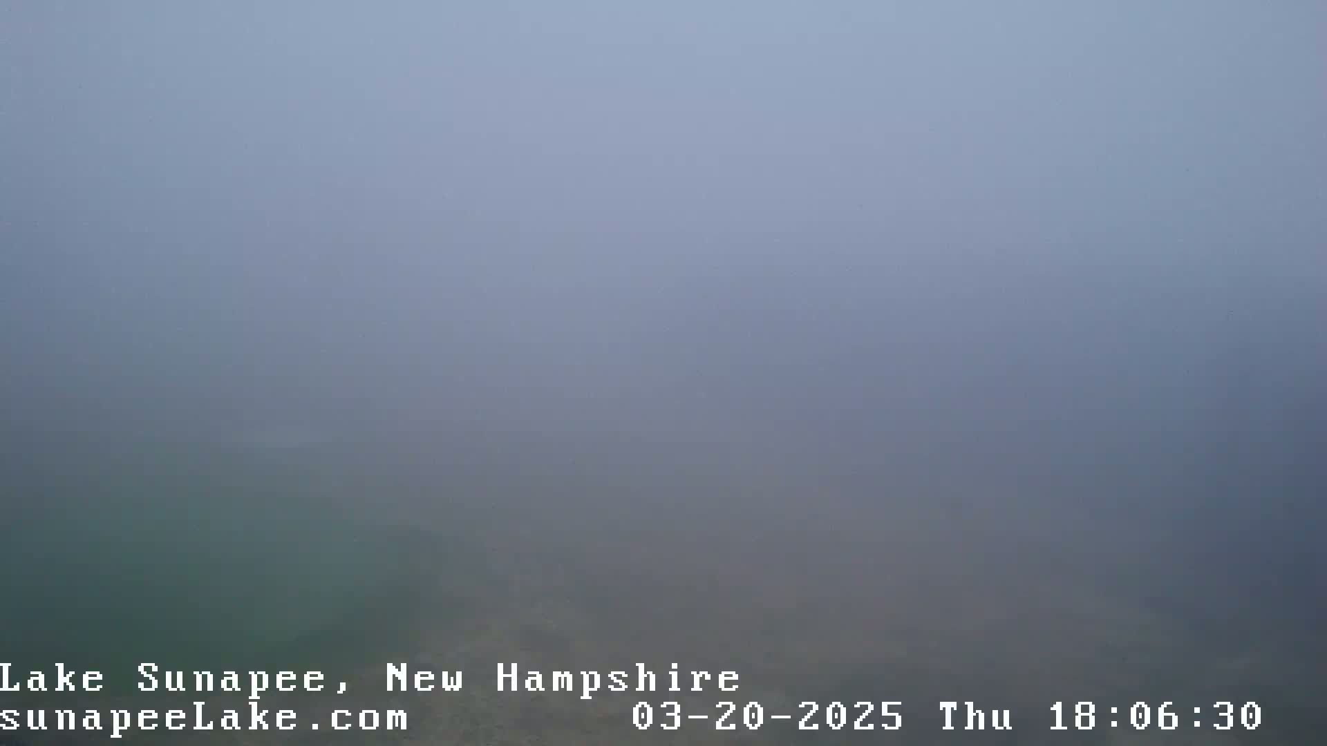 A thick fog obscures the view of a body of water.
