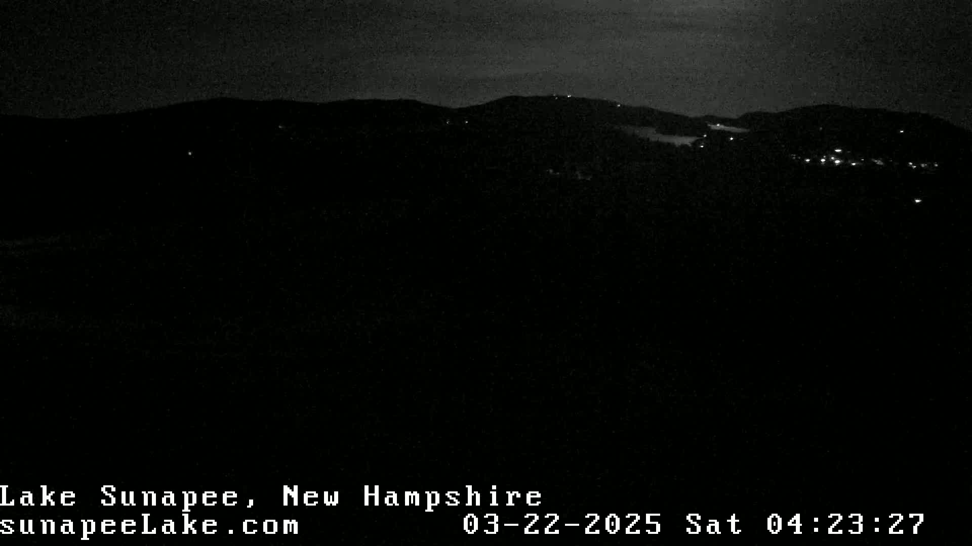 A nighttime, long-range view of dark hills and sparsely lit structures under a clear, dark sky.