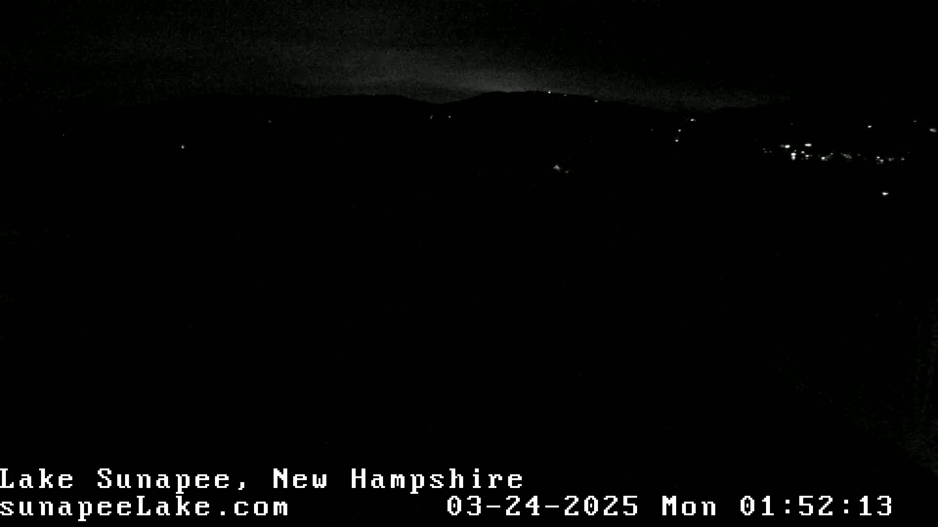 A nighttime view of a dark landscape with a few distant lights visible under a mostly clear sky.
