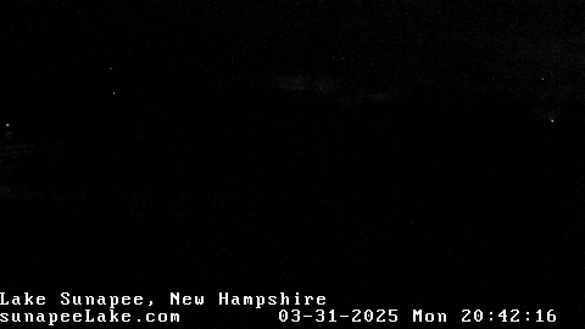 A nearly entirely black image shows a few faint lights in the night sky.