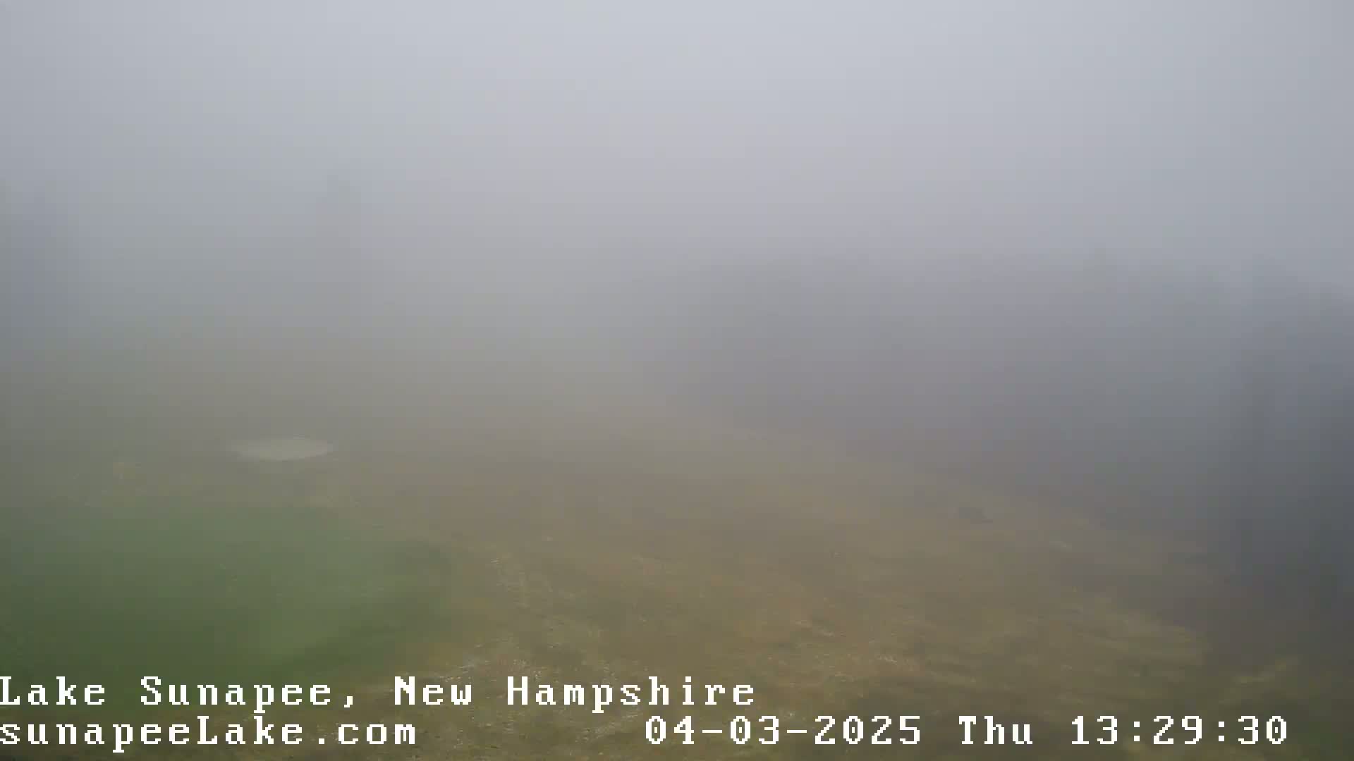 A foggy, low-visibility scene shows a body of water and land shrouded in mist.