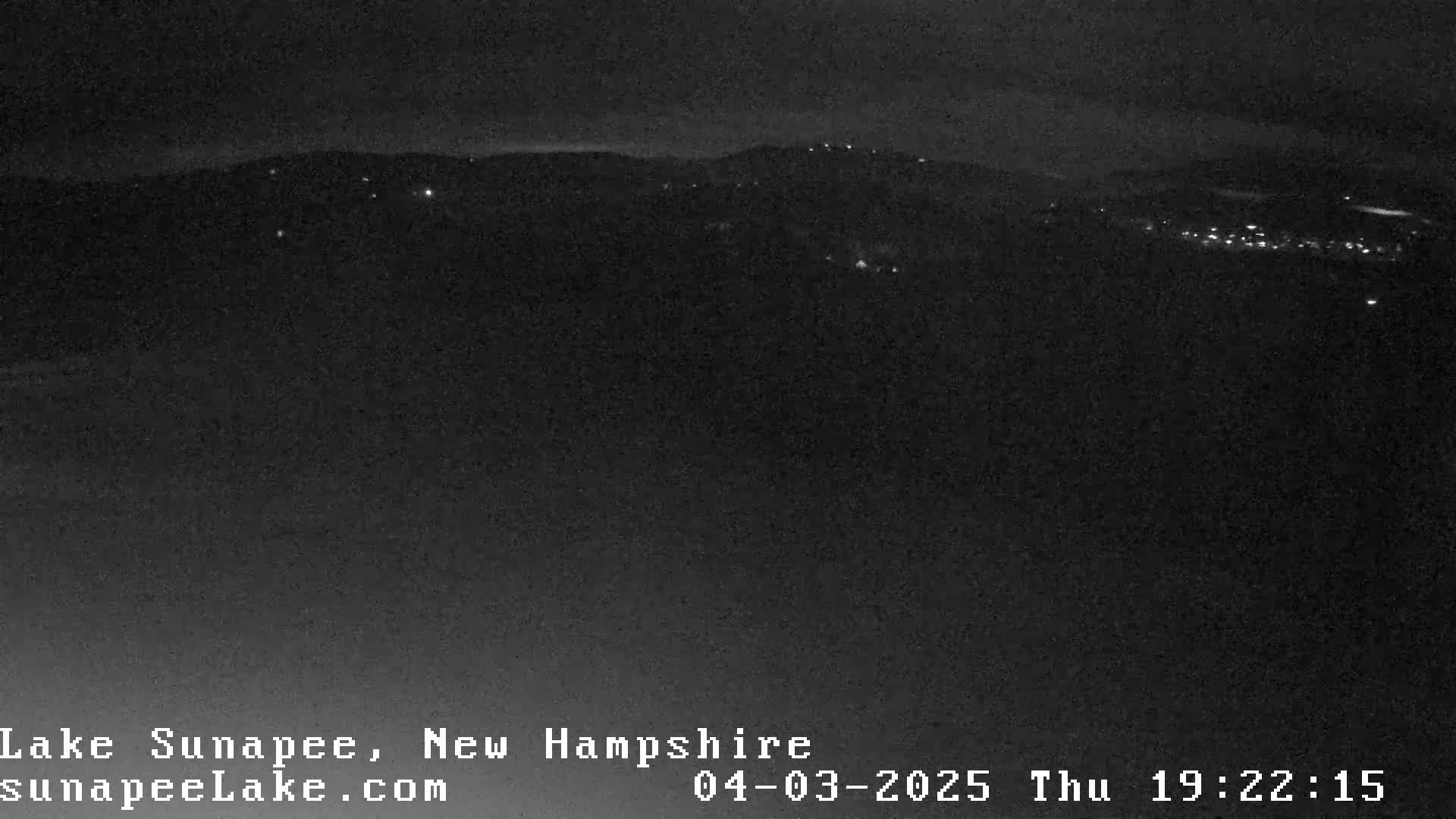 A nighttime long shot shows a dark landscape with a few distant lights scattered across hills.