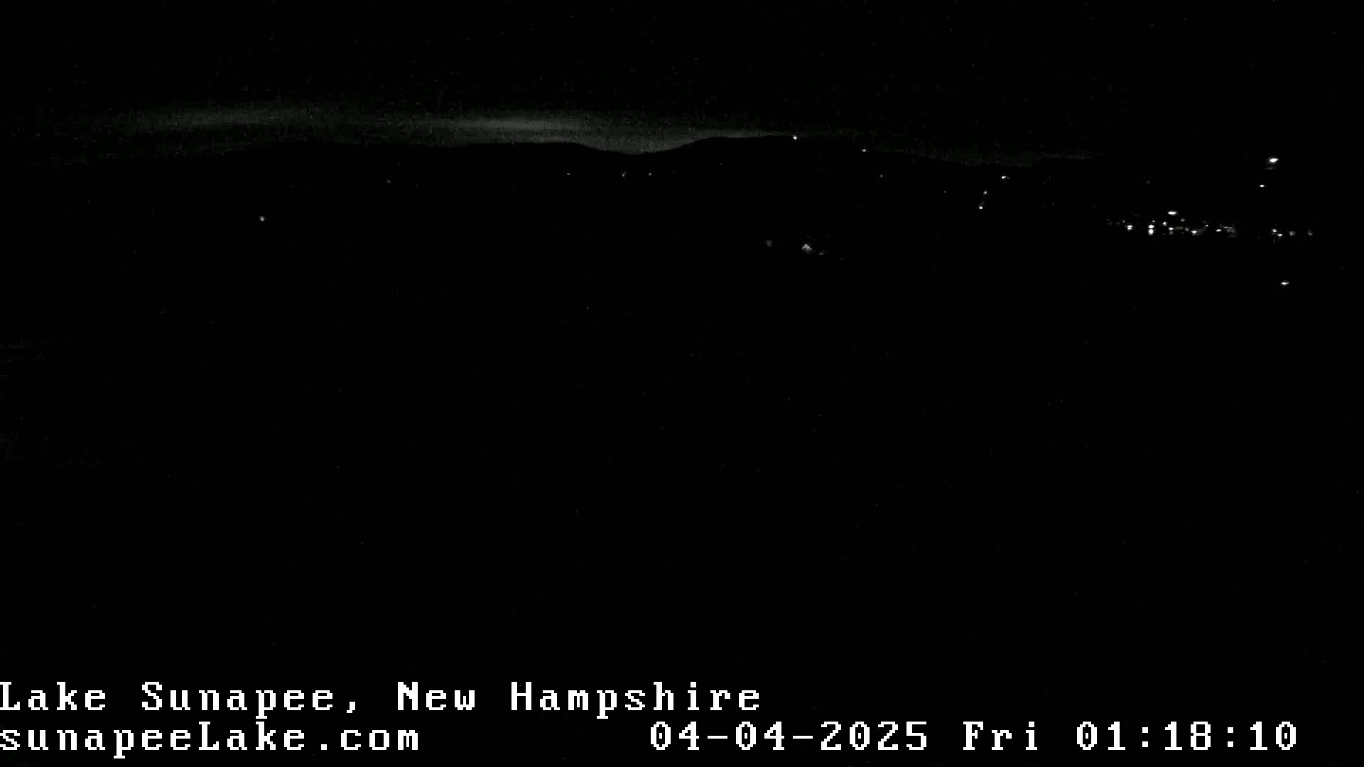 A nighttime long shot shows a dark landscape with a few distant lights and a barely visible horizon under a dark sky.