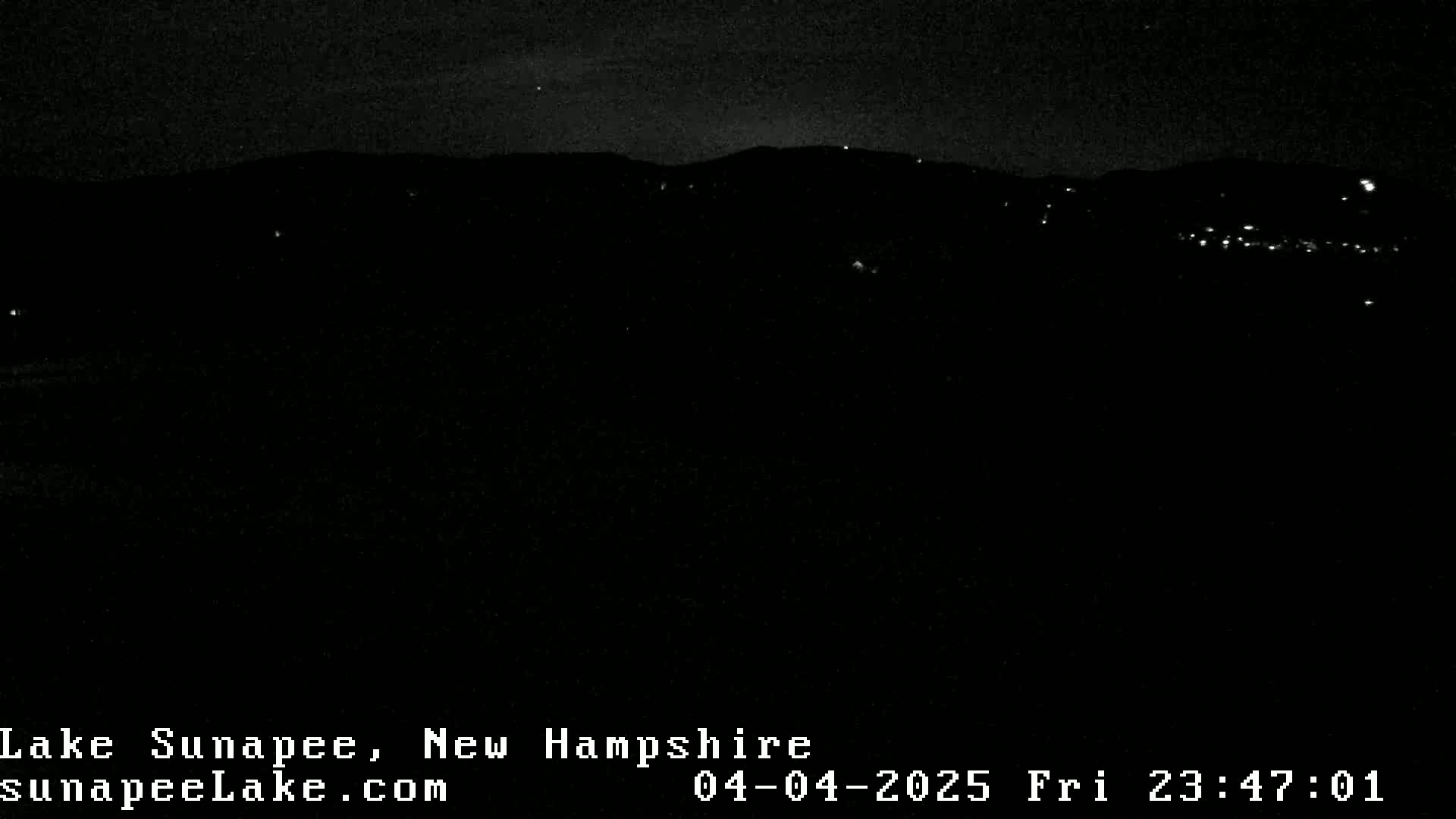 A nighttime, low-light view of a dark landscape with a few distant lights visible.