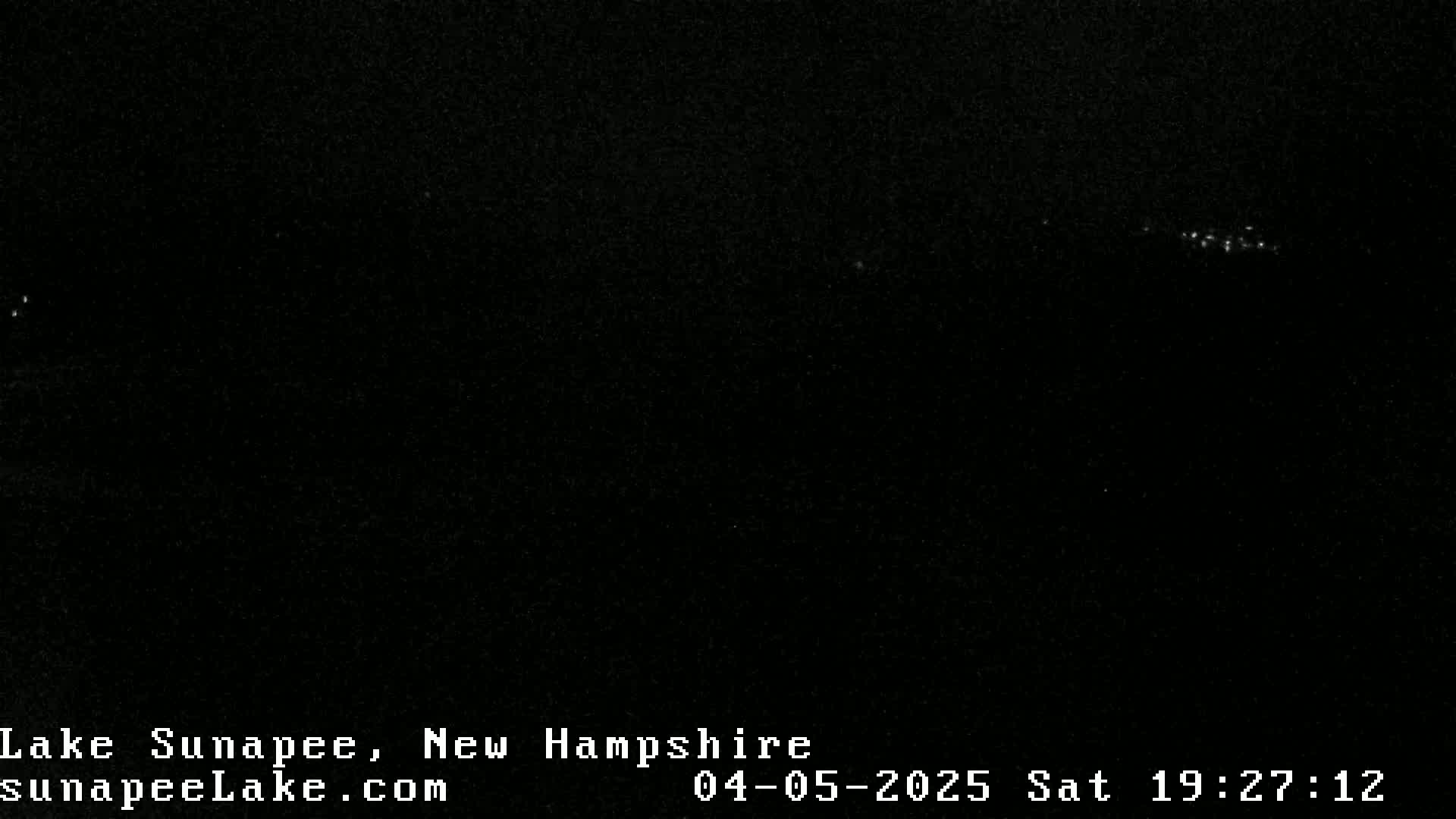 A nighttime image shows a dark, possibly water-covered area with a few distant lights visible in the darkness.