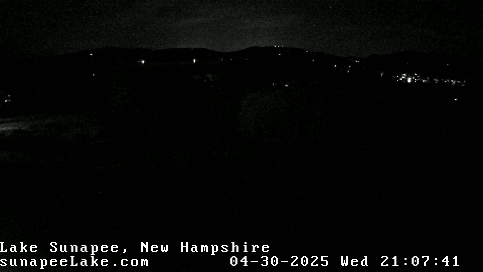 A nighttime view of a dark landscape with sparsely scattered lights in the distance under a clear, dark sky.