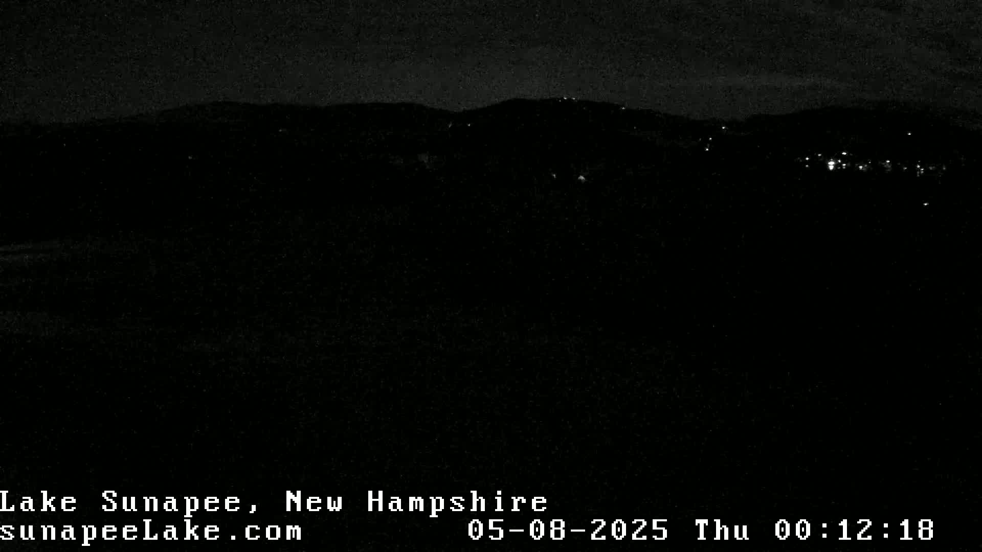 A nighttime view of dark hills and a few distant lights under a clear, dark sky.