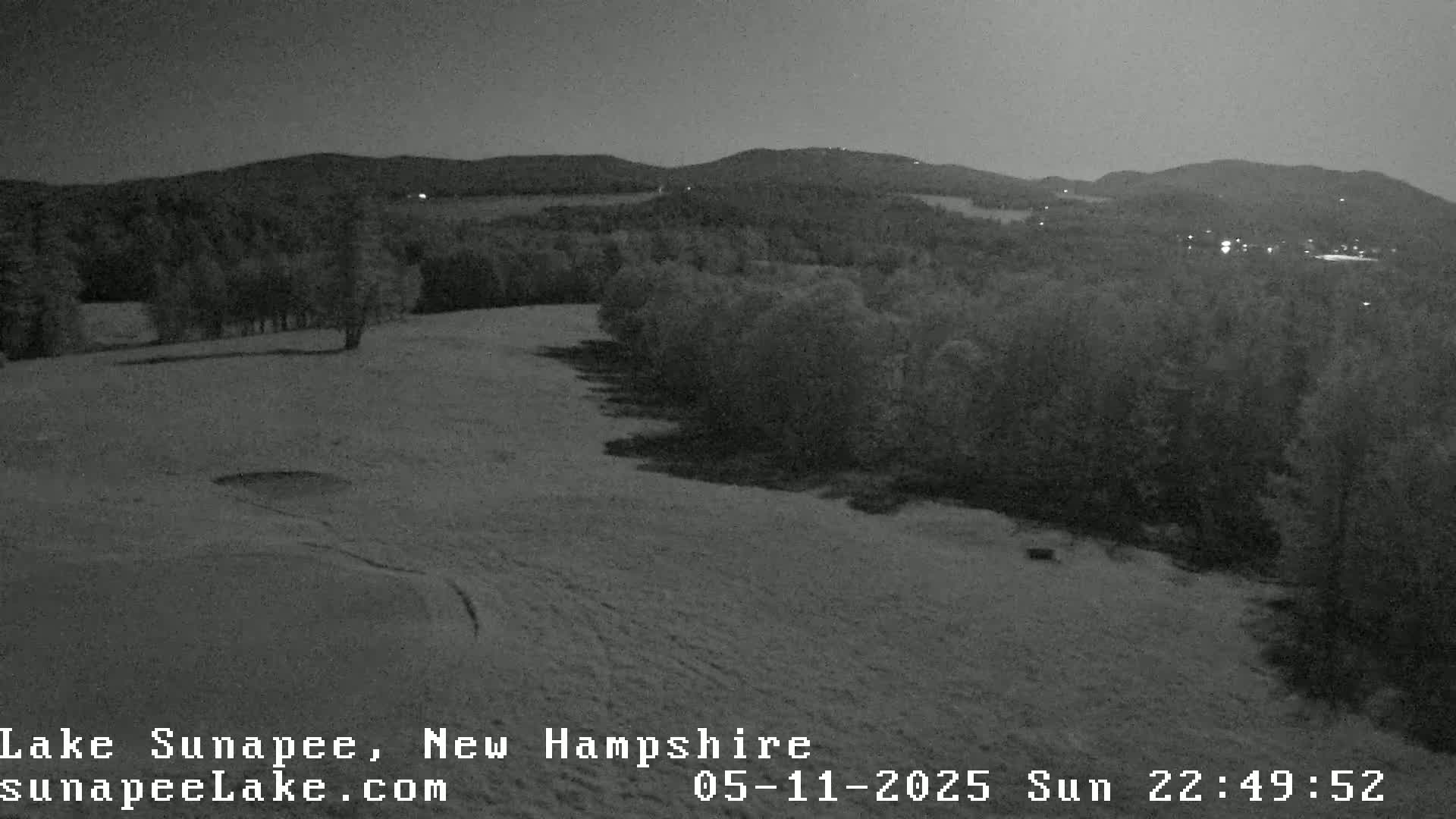 A nighttime, snow-covered field slopes down toward a dark line of trees under a dim sky.