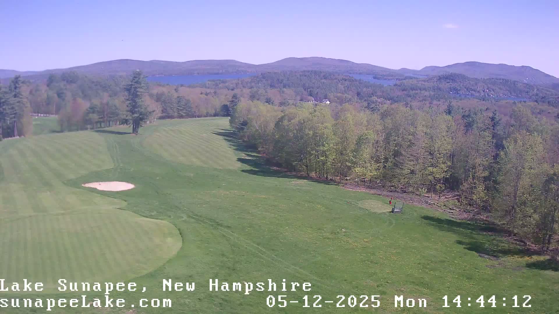 A sunny view of a golf course with a lake and mountains in the background.