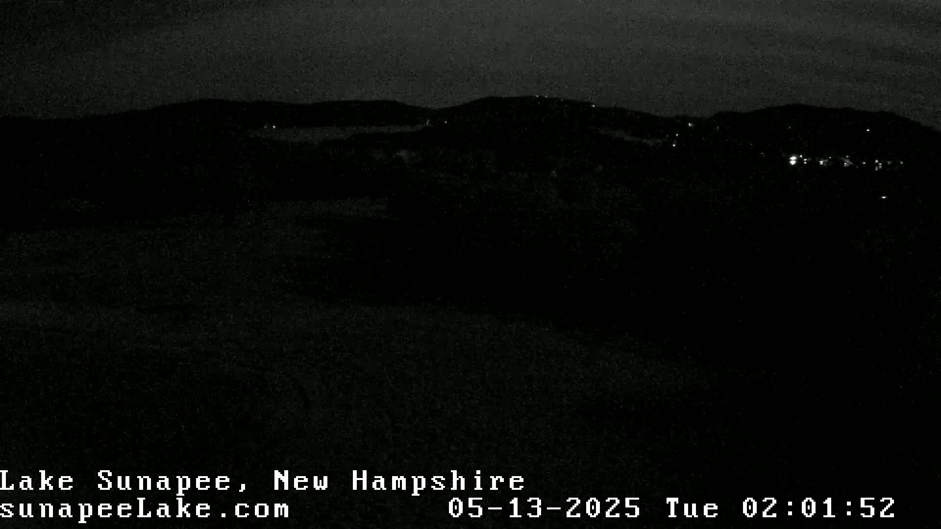 A dark, nighttime view of a hilly landscape with a few distant lights.