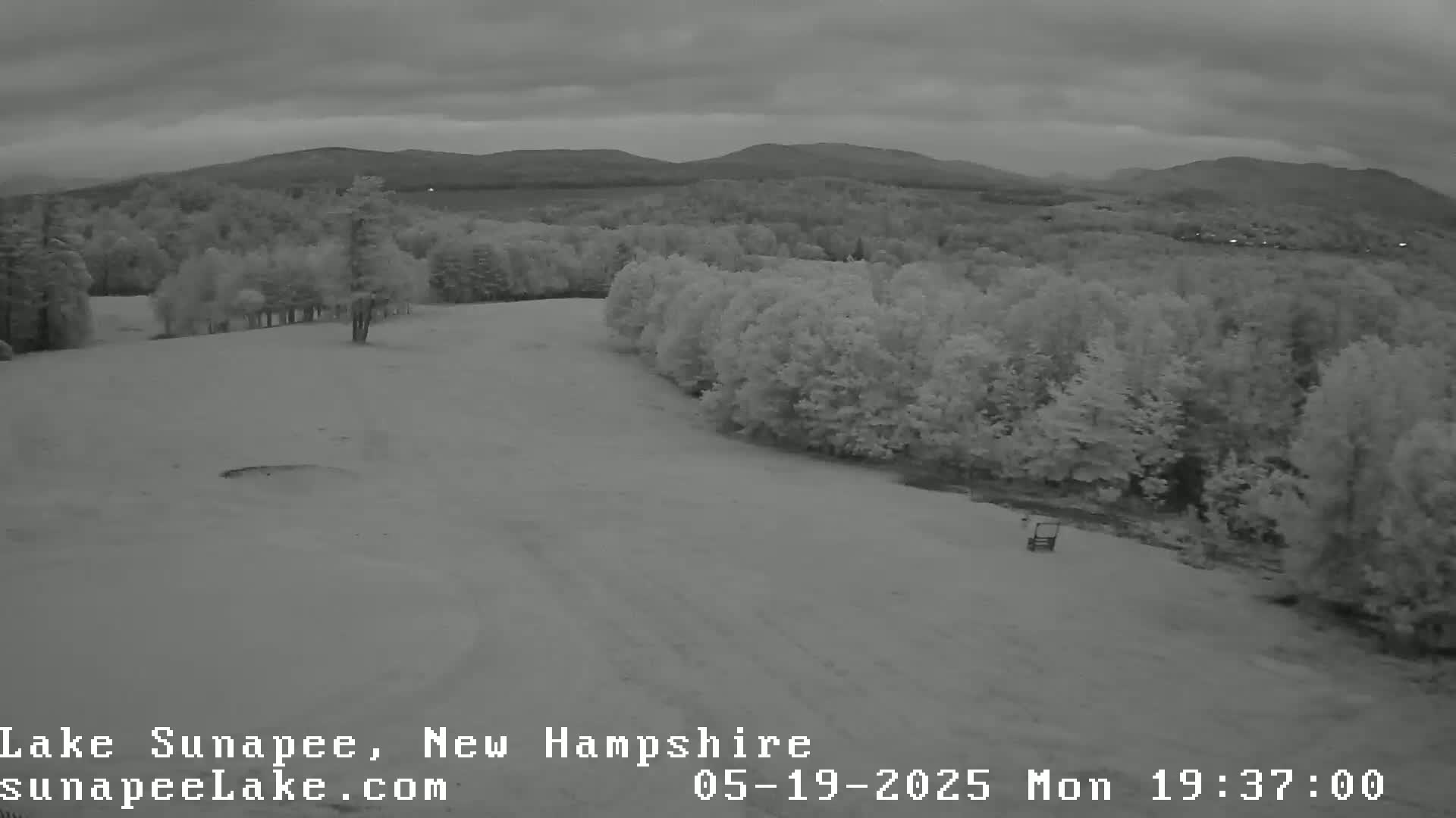A mostly cloudy, overcast day shows a snow-covered landscape with trees and distant mountains.