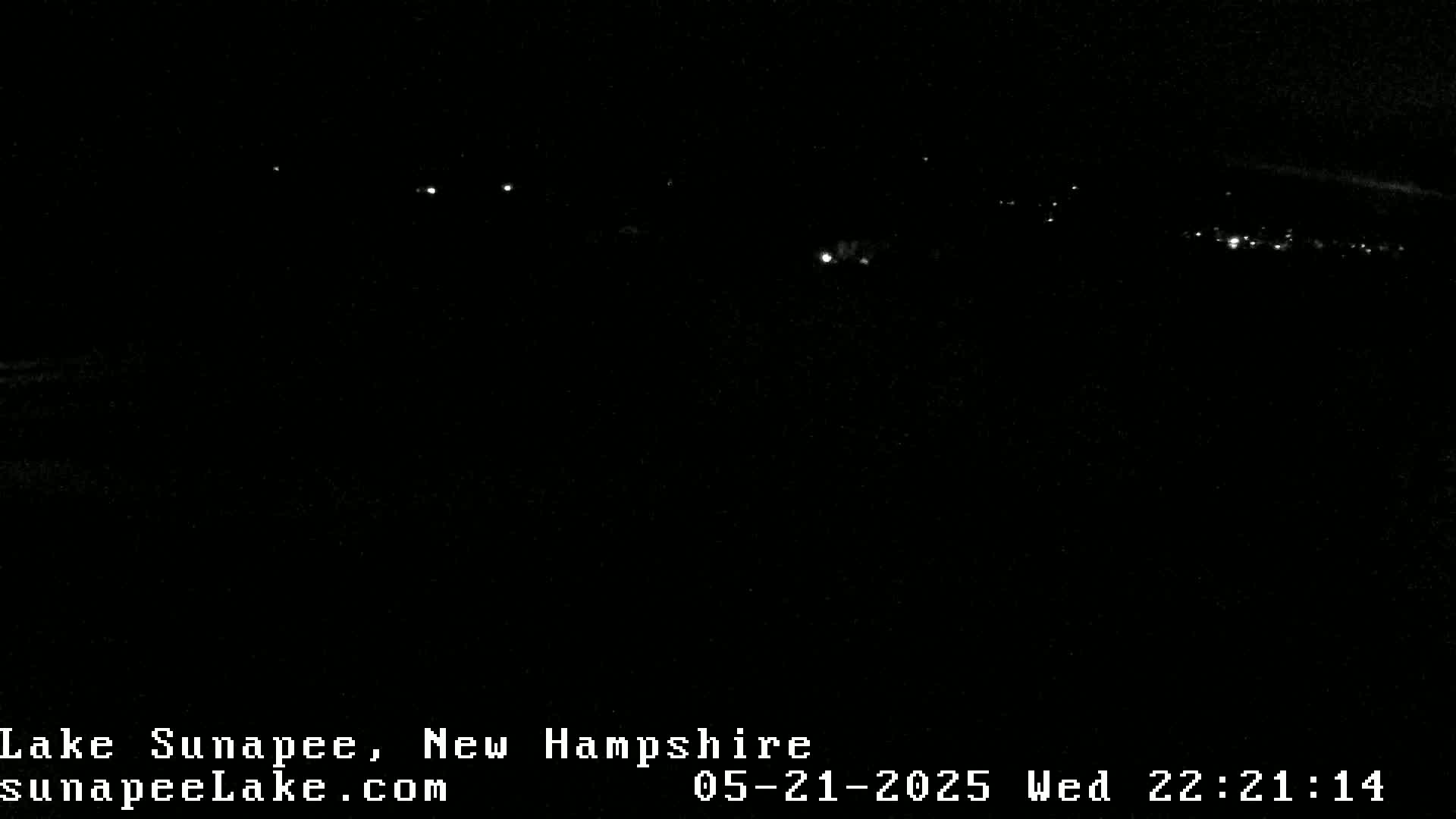A nighttime, low-light view of distant lights possibly from a town or city across a dark body of water.