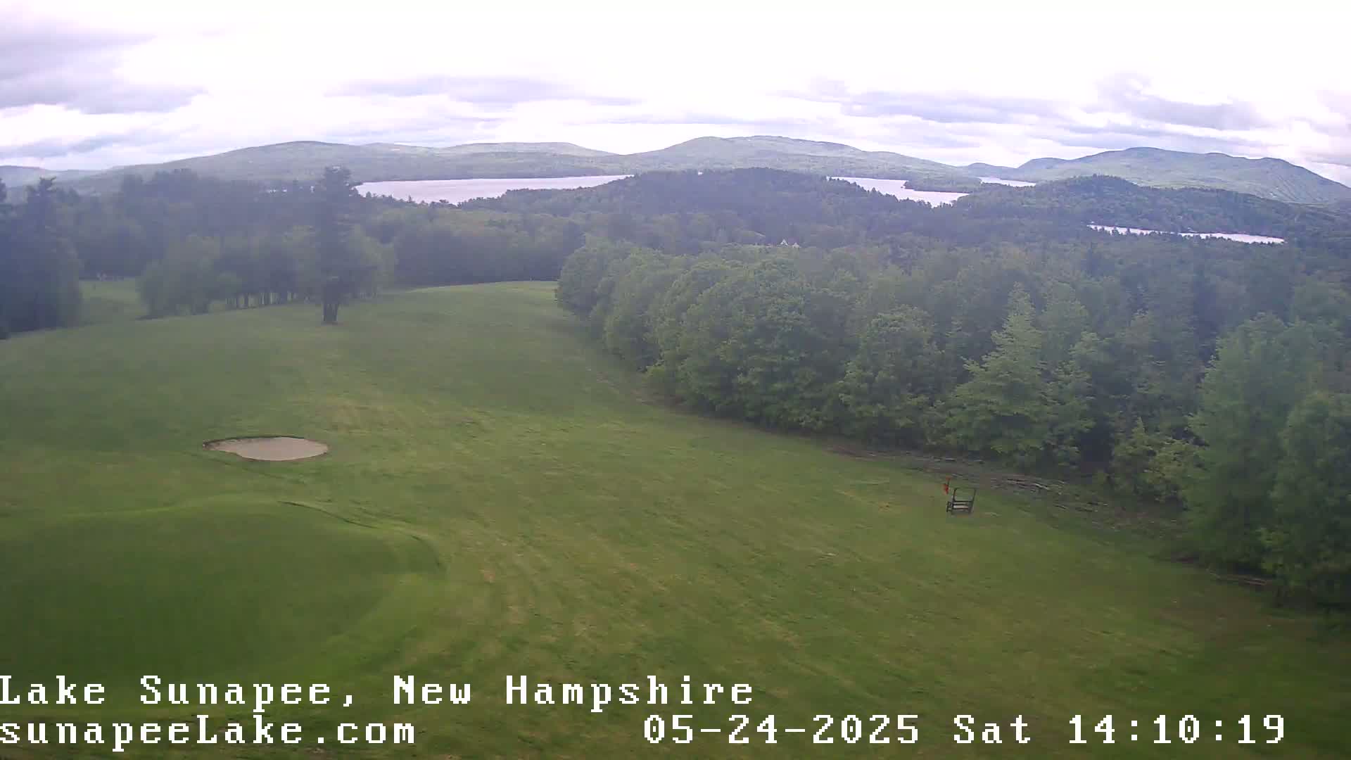 An elevated view shows a green golf course with a sand trap and distant lakes under a cloudy sky.