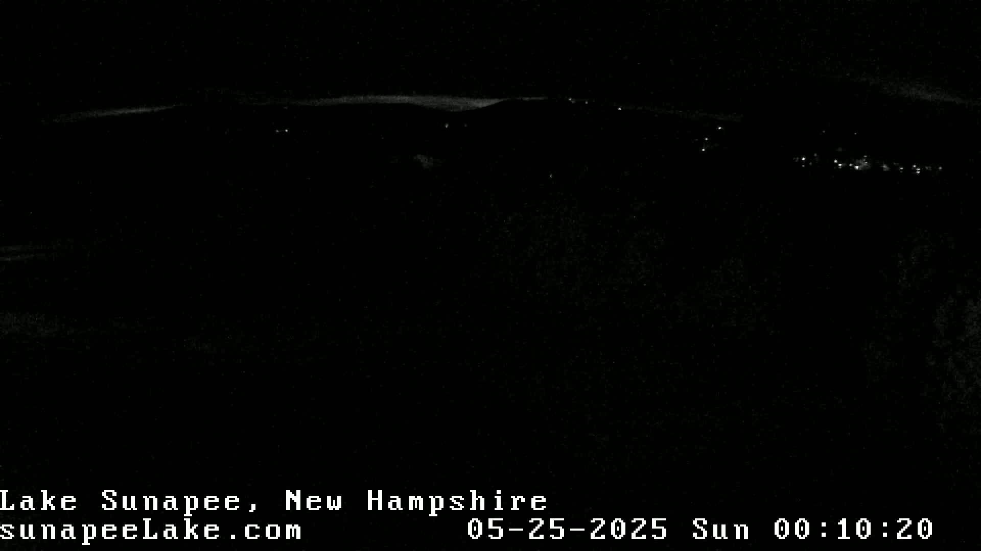 A nighttime, long-range view of a dark landscape with a few distant lights.