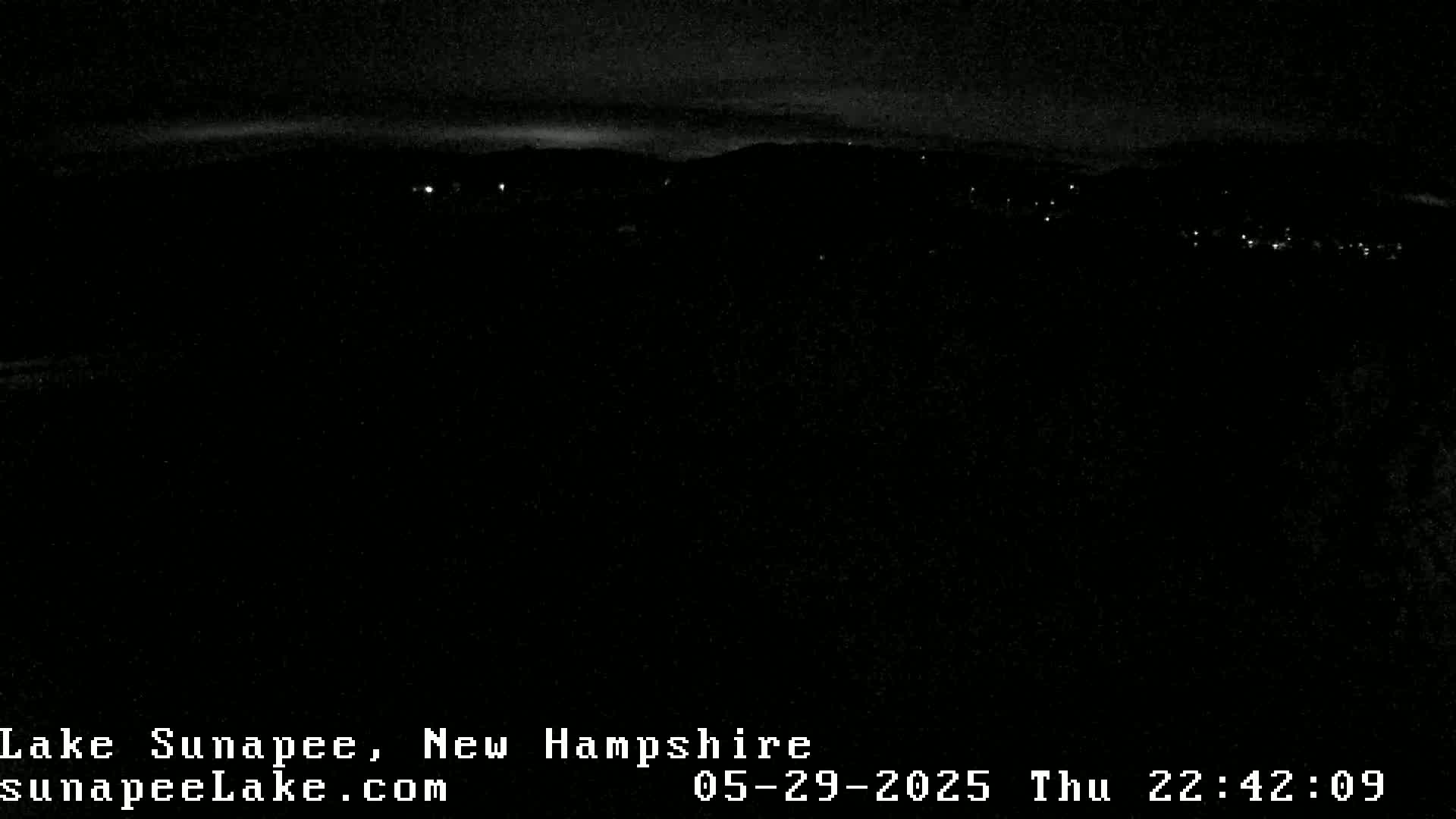 A dark nighttime scene shows a distant line of lights against a dark mountain range under a mostly clear sky.