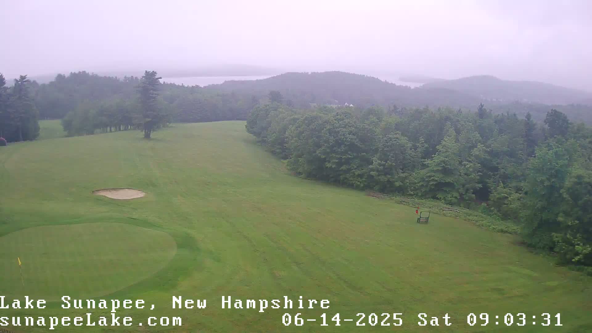 A golf course with a sand trap and distant lake is visible on an overcast day.