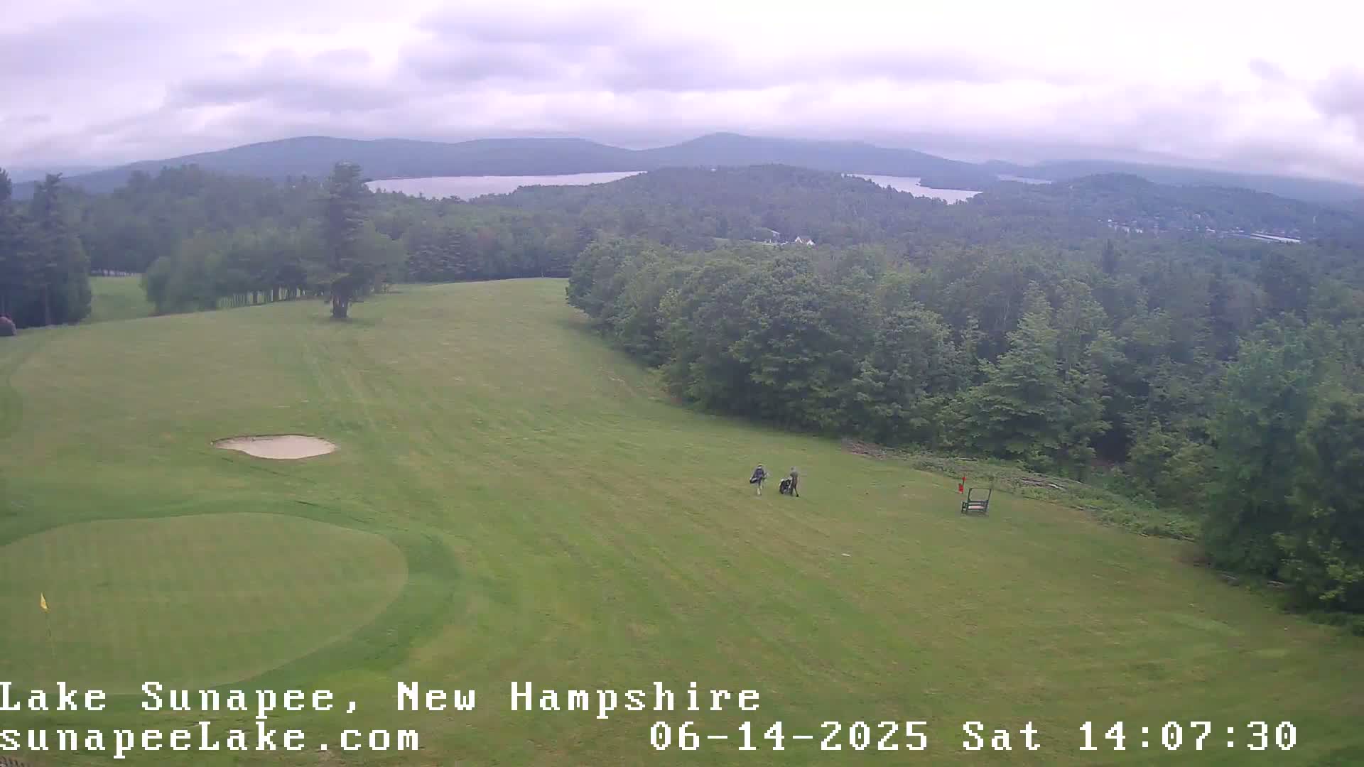 A golf course with a sand trap and distant lake is visible on an overcast day.