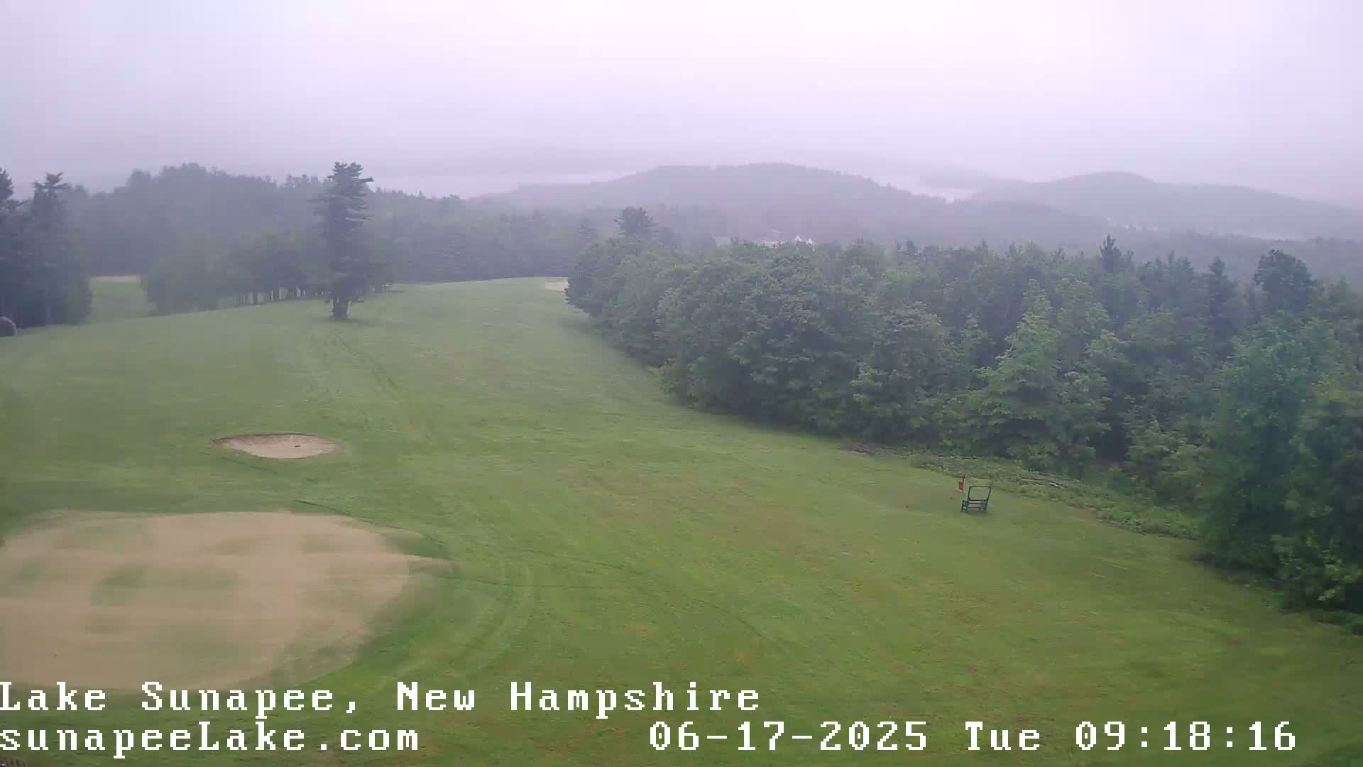 A golf course with sand traps is visible, bordered by a dense forest under an overcast sky.