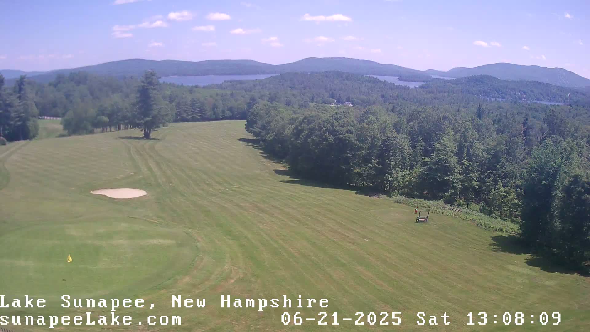 A golf course fairway overlooks a lake and mountains under a clear, sunny sky.