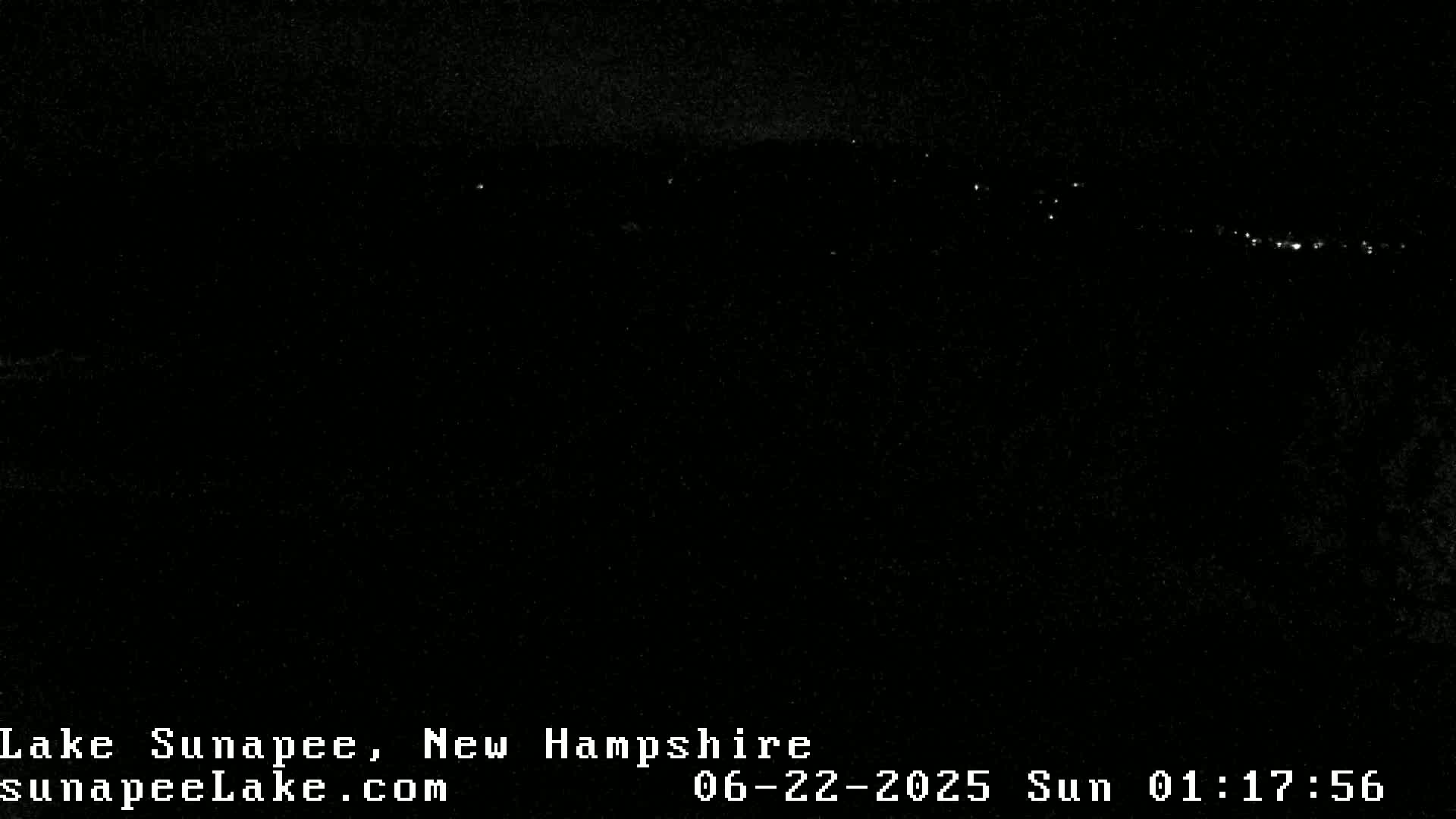 A nighttime view shows a distant line of lights on a hill under a dark, clear sky.