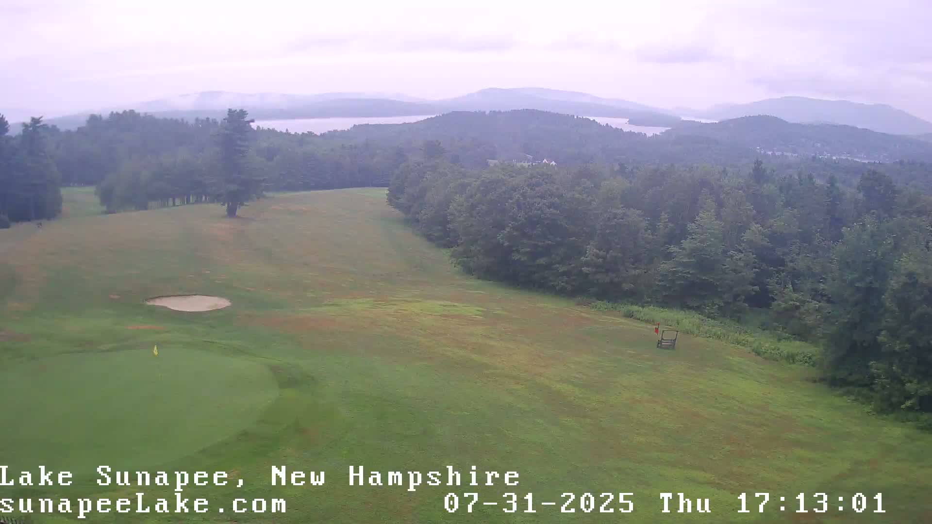 A golf course with a putting green and distant lake is visible under an overcast sky.