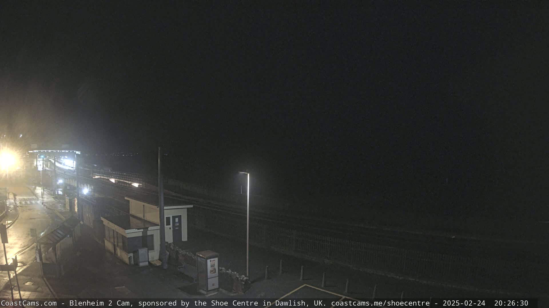 A nighttime view of a coastal train station and adjacent beach area under a dark, clear sky.
