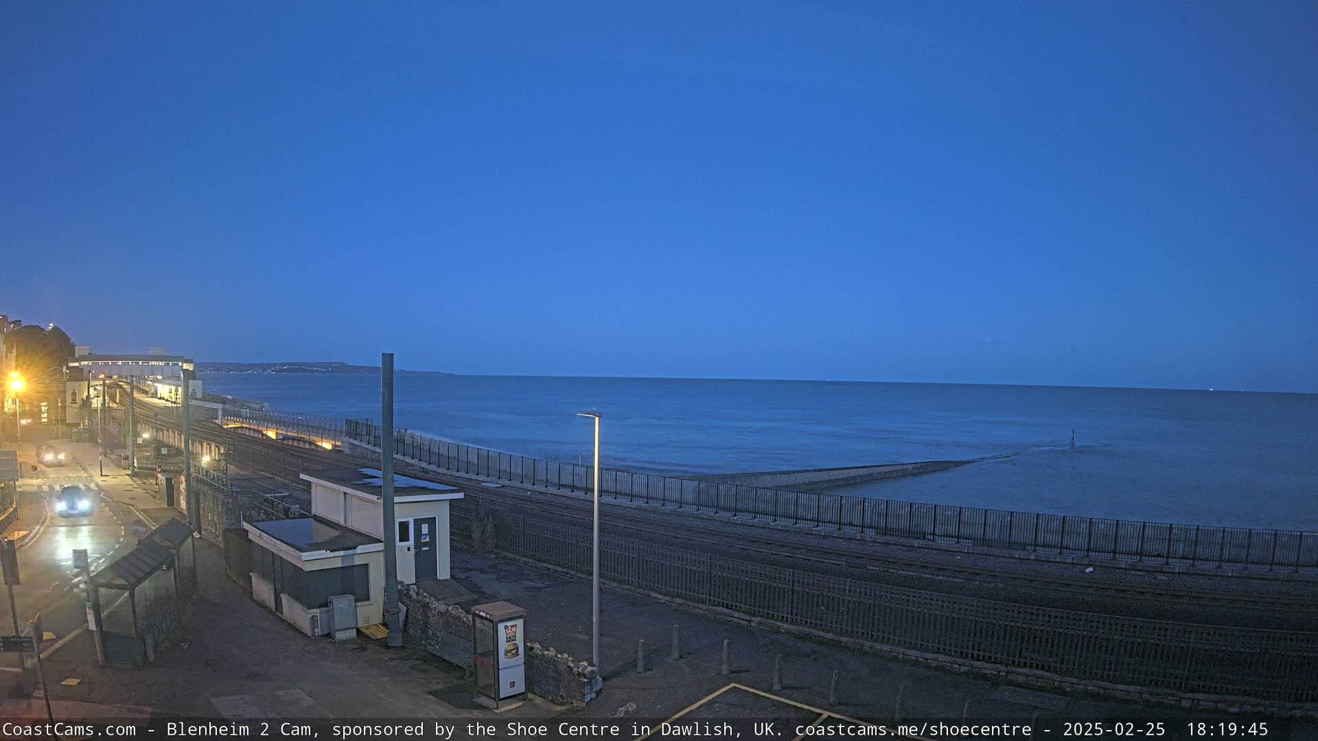 A coastal railway line runs alongside a dark, calm sea under a twilight blue sky.