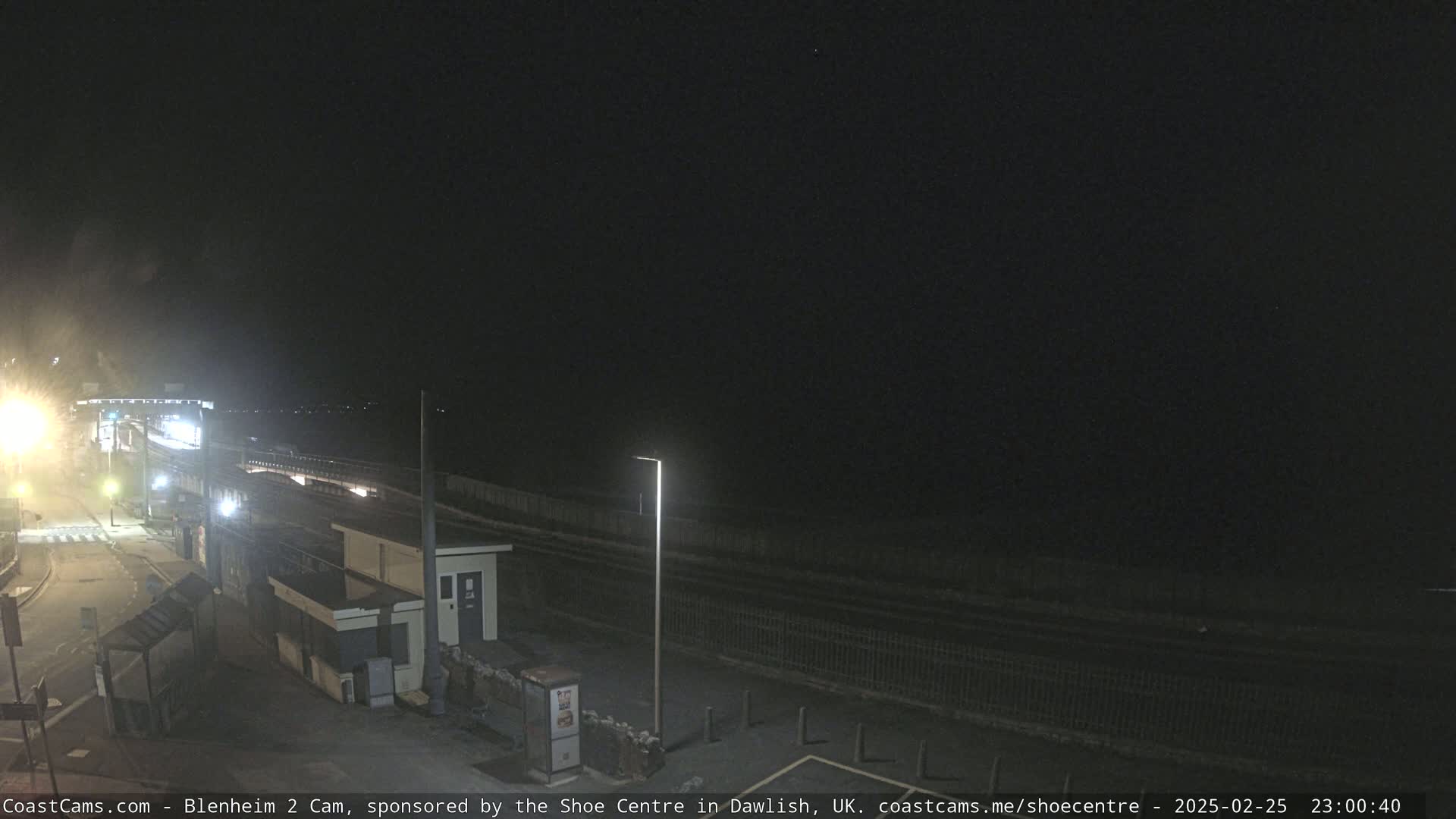 A nighttime view of a coastal road and buildings under a dark, clear sky.