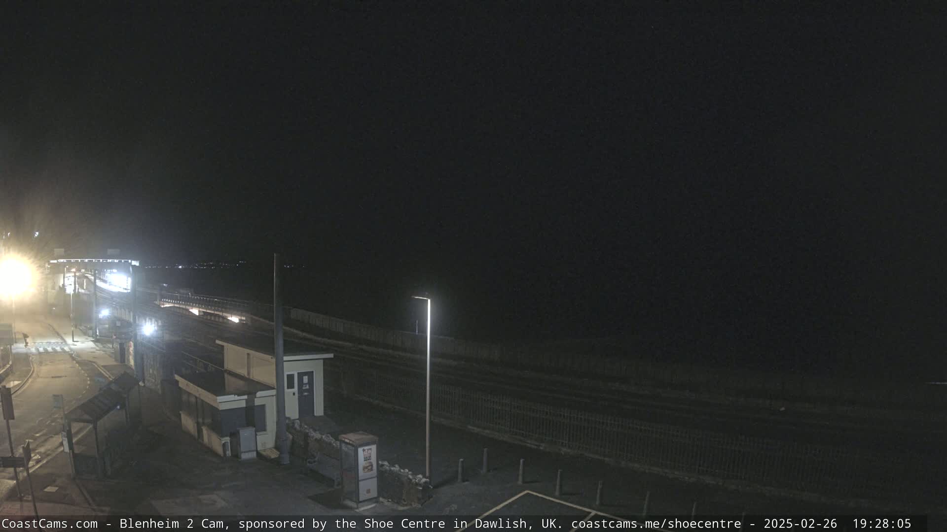 A nighttime, outdoor view of a train station platform and surrounding area, illuminated by artificial lights.